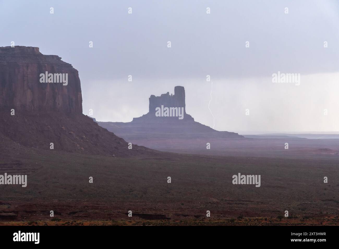 Une scène dramatique capture un éclair éclatant frappant près des formations rocheuses emblématiques de Monument Valley au milieu d'une tempête violente, sous un ciel sombre Banque D'Images