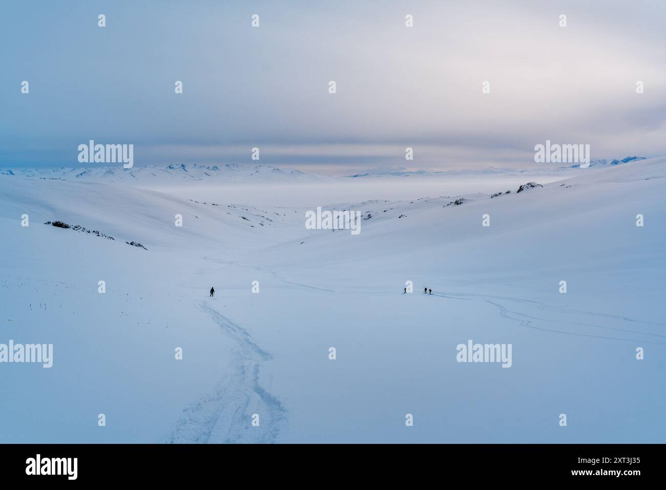 Des personnages méconnaissables traversent un immense paysage enneigé sous un vaste ciel au Kirghizistan, leurs chemins marqués par des empreintes de pas dans la neige immaculée. Banque D'Images