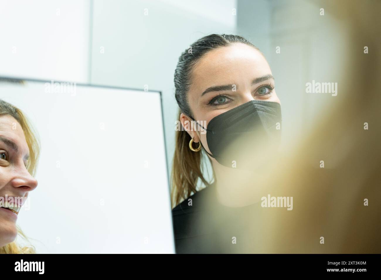 Cette image capture une esthéticienne portant un masque et un client examinant les résultats d'une procédure de microblading dans un miroir. La scène met en évidence les s. Banque D'Images