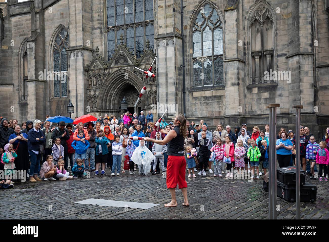 Edinburgh Festival Fringe, Royal Mile Édimbourg, Écosse, Royaume-Uni, 13 août 2024. Vents bruyants et rafales pour le deuxième mardi sur la High Street, une fois de plus les conditions météorologiques amenant les artistes de rue à varier et à modifier leurs routines normales pour leur permettre de continuer leurs spectacles. Sur la photo : Mulletman et MIM de Nouvelle-Zélande divertissent le public sur la place du Parlement avec des compétences de tir à l'arc MIMS visant un club de jonglage au jongleur Mulletmans . Credit : Arch White/Alamy Live news. Banque D'Images