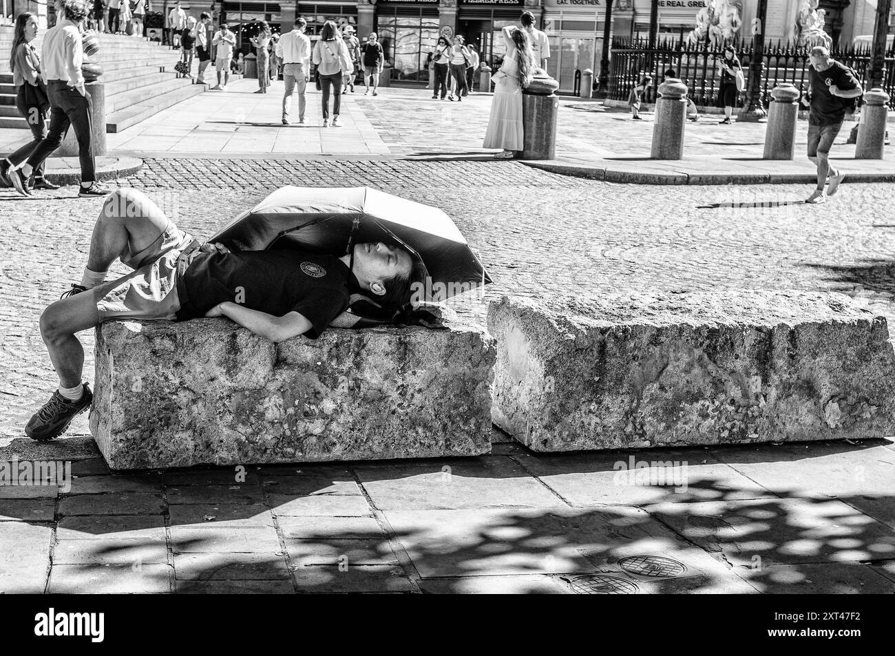 Touriste pris en charge par la chaleur se couche sur des pierres situées autour de la cathédrale St Paul et utilise un parapluie de couleurs vives pour se faire de l'ombre. Banque D'Images