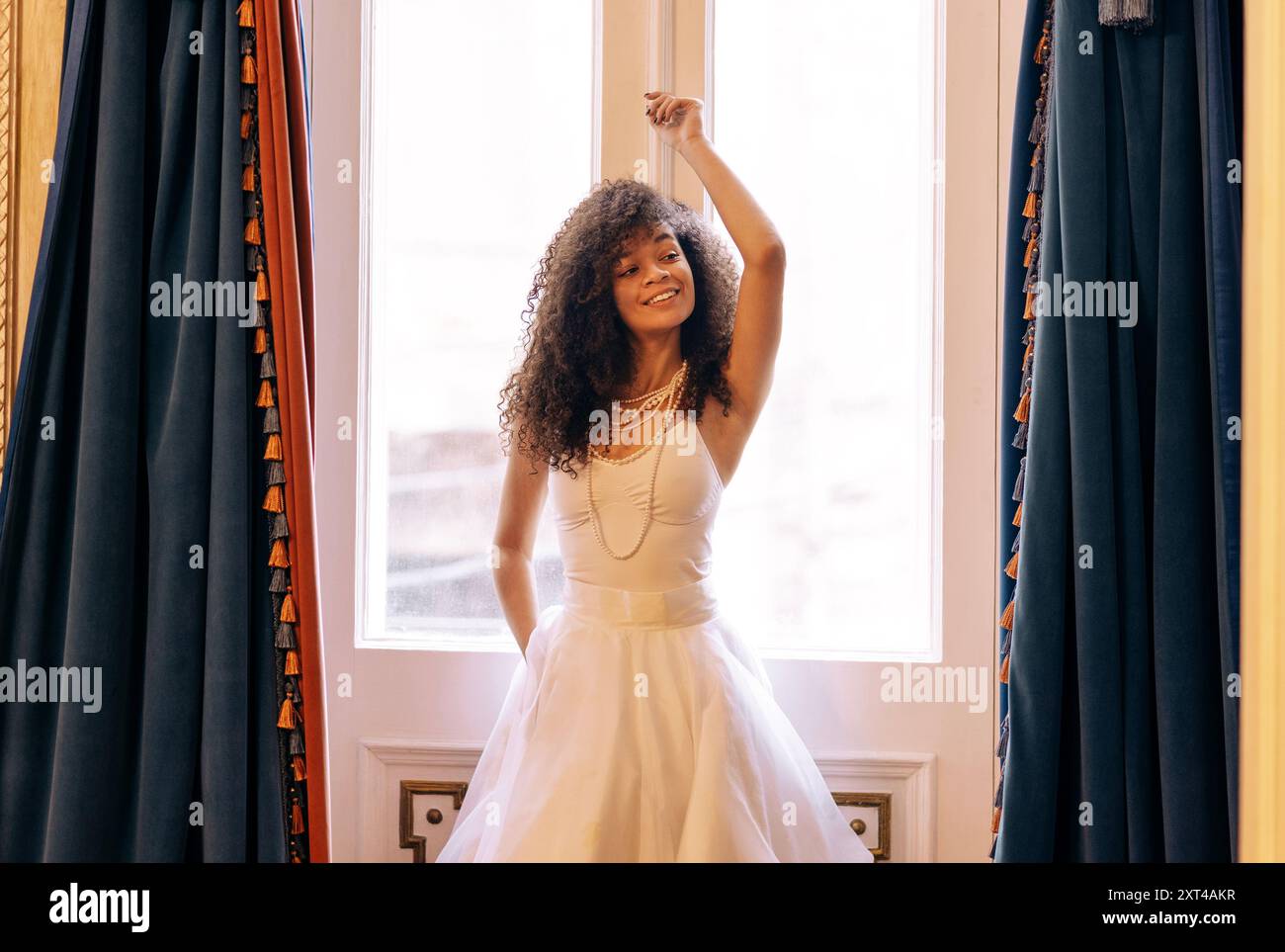 Charmante femme africaine aux cheveux bouclés dans une élégante robe blanche se tient près des portes rétro décorées et se tient sur le cadre. Jolie fille noire porte perle j Banque D'Images
