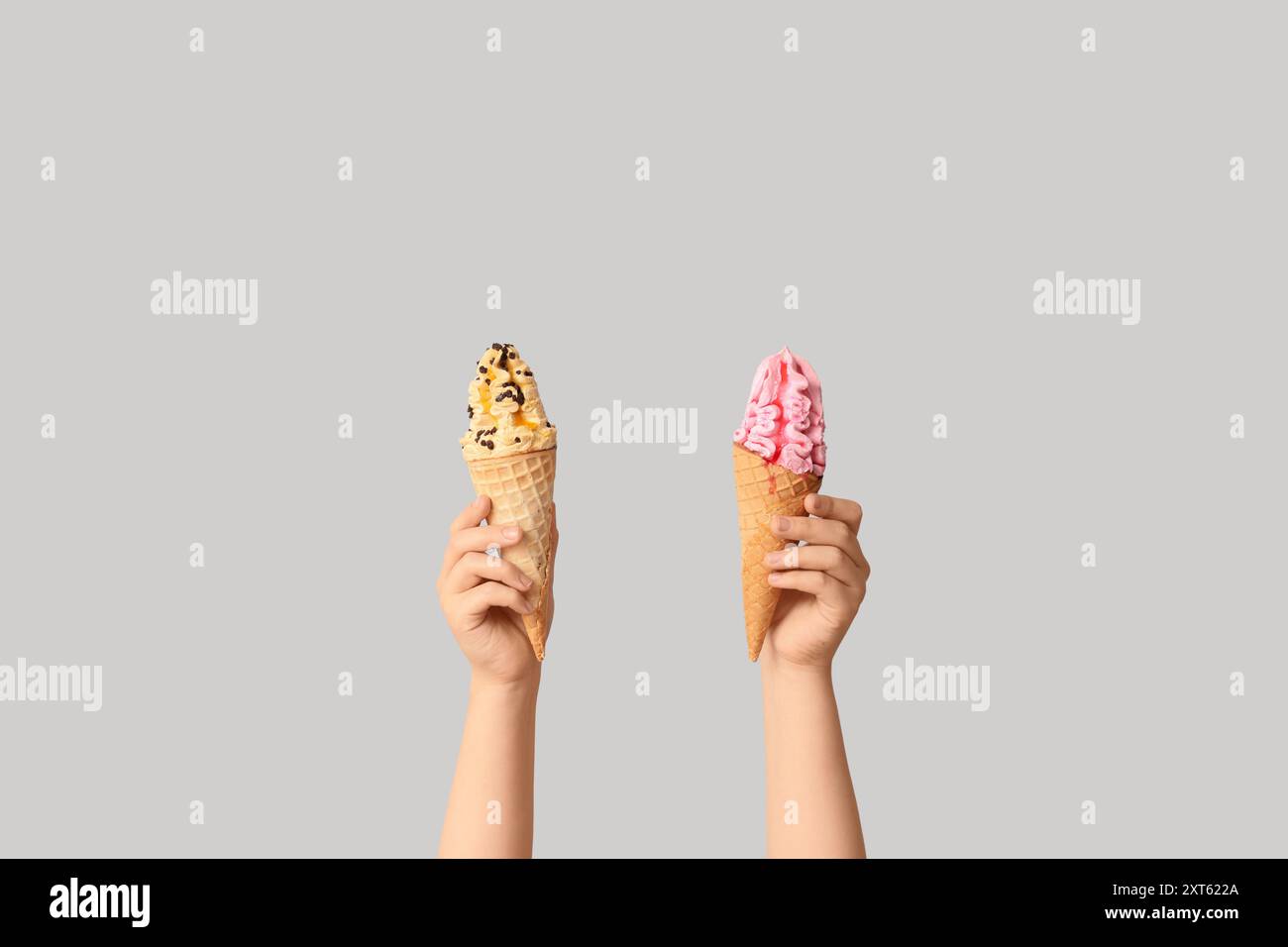 Mains féminines avec différentes glaces sucrées en cônes gaufrés sur fond gris Banque D'Images