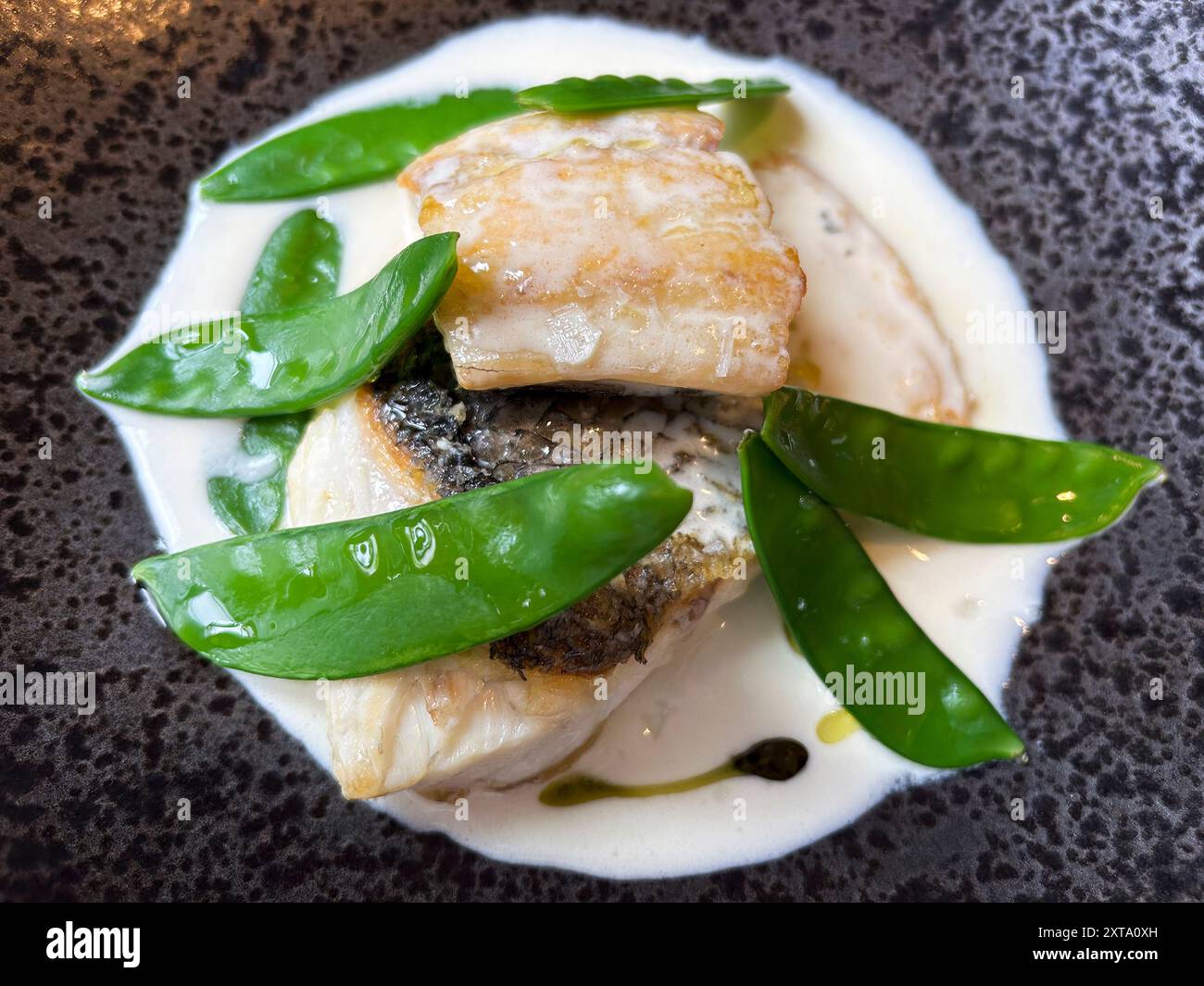 Vue de dessus d'un plat cuit de poisson avec des pois mange-tout, présenté sur une assiette blanche. Banque D'Images