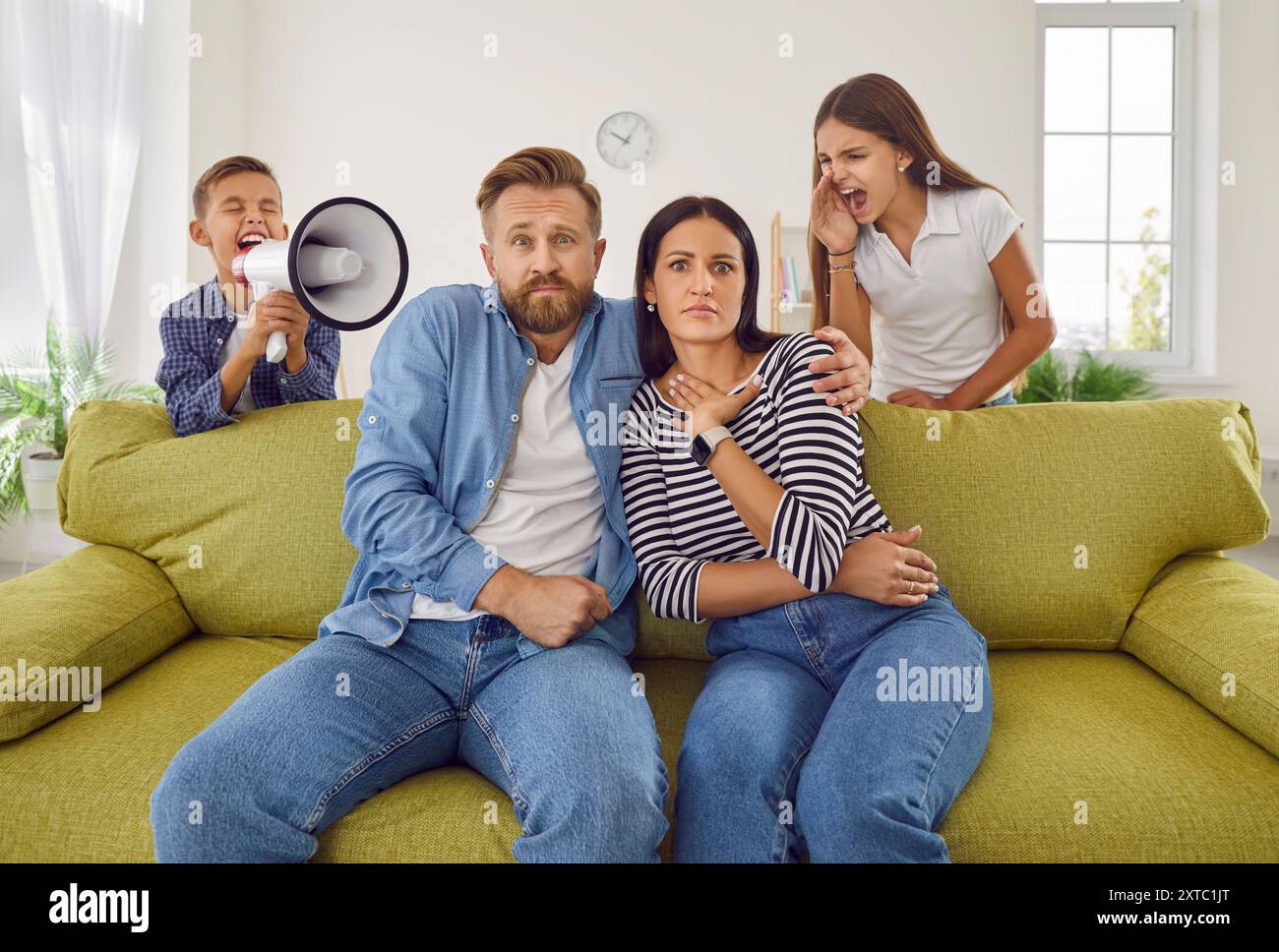 Mère et père fatigués assis sur le canapé à la maison tandis que des enfants bruyants crient dans le haut-parleur. Banque D'Images