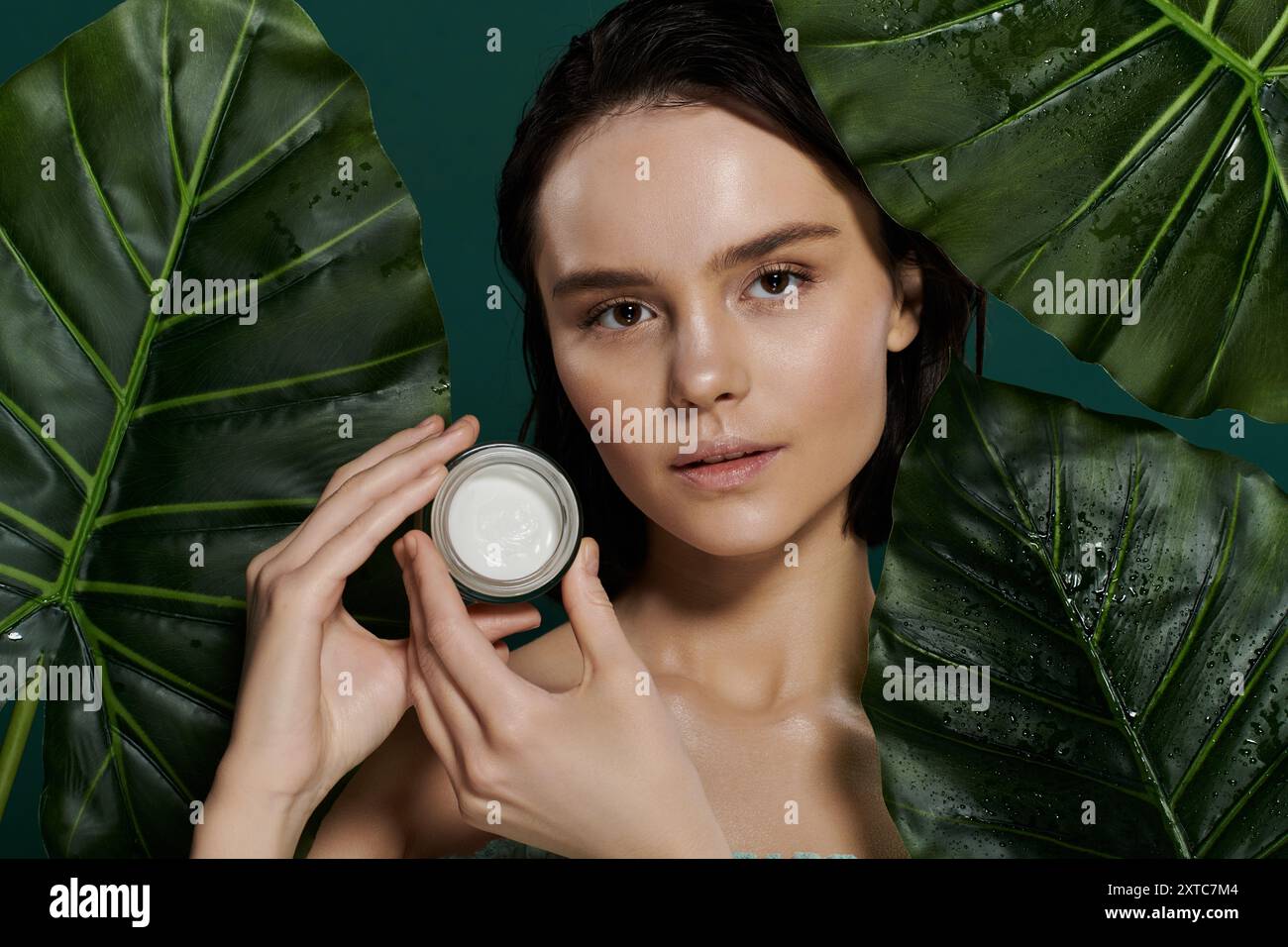 Une femme pose avec un pot de crème devant un fond vert éclatant. Banque D'Images