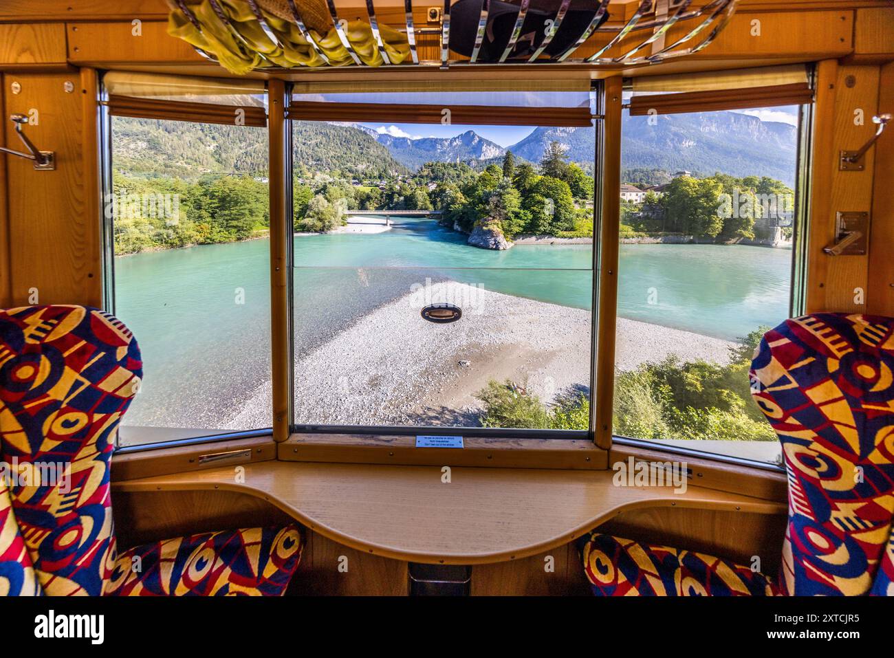 De la fenêtre du compartiment du Pullman Express Alpine Classic à l’arrêt, la vue s’ouvre sur la confluence du Vorderrhein et du Hinterrhein près de Reichenau, une berge de gravier marquant le point où les deux rivières se rejoignent. Le train date de 1931 et circulait à l’origine sous le nom de 'Golden Mountain Pullman Express' sur la ligne ferroviaire Montreux–Berner Oberland. Le chemin de fer rhétique l’a acheté en 1939 et l’a utilisé pour les voyages d’inspection de l’armée de 1940 jusqu’à la fin de la guerre. Le Verein Pro Salonwagen, fondé en 1998, a sauvé le train, qui est aujourd’hui un monument ferroviaire historique protégé en t Banque D'Images