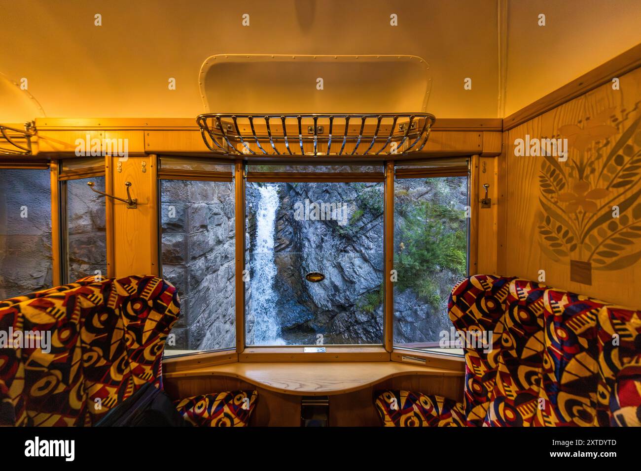 Une cascade plonge une paroi rocheuse derrière la fenêtre panoramique d'un wagon du Alpine Classic Pullman Express. Le train date de 1931 et circulait à l'origine sous le nom de 'Golden Mountain Pullman Express' sur la ligne ferroviaire Montreux–Oberland bernois. Le chemin de fer rhétique l'a acheté en 1939 et l'a utilisé pour des voyages d'inspection de l'armée de 1940 jusqu'à la fin de la guerre. Le designer français René Prou avait créé les incrustations en bois et la garniture Art Déco des wagons. Le Verein Pro Salonwagen, fondé en 1998, a sauvé le train, qui est aujourd'hui un monument ferroviaire historique protégé dans le canton des Grisons Banque D'Images