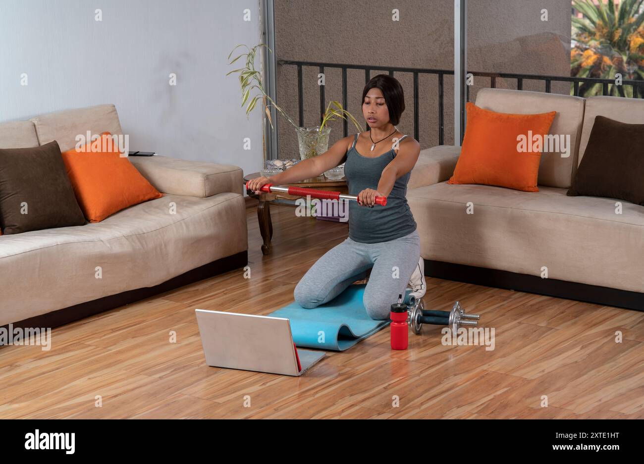 Jeune femme afro-américaine s'exerçant dans son salon portant des vêtements de sport à côté de son ordinateur portable, guidée par un tutoriel en ligne Banque D'Images