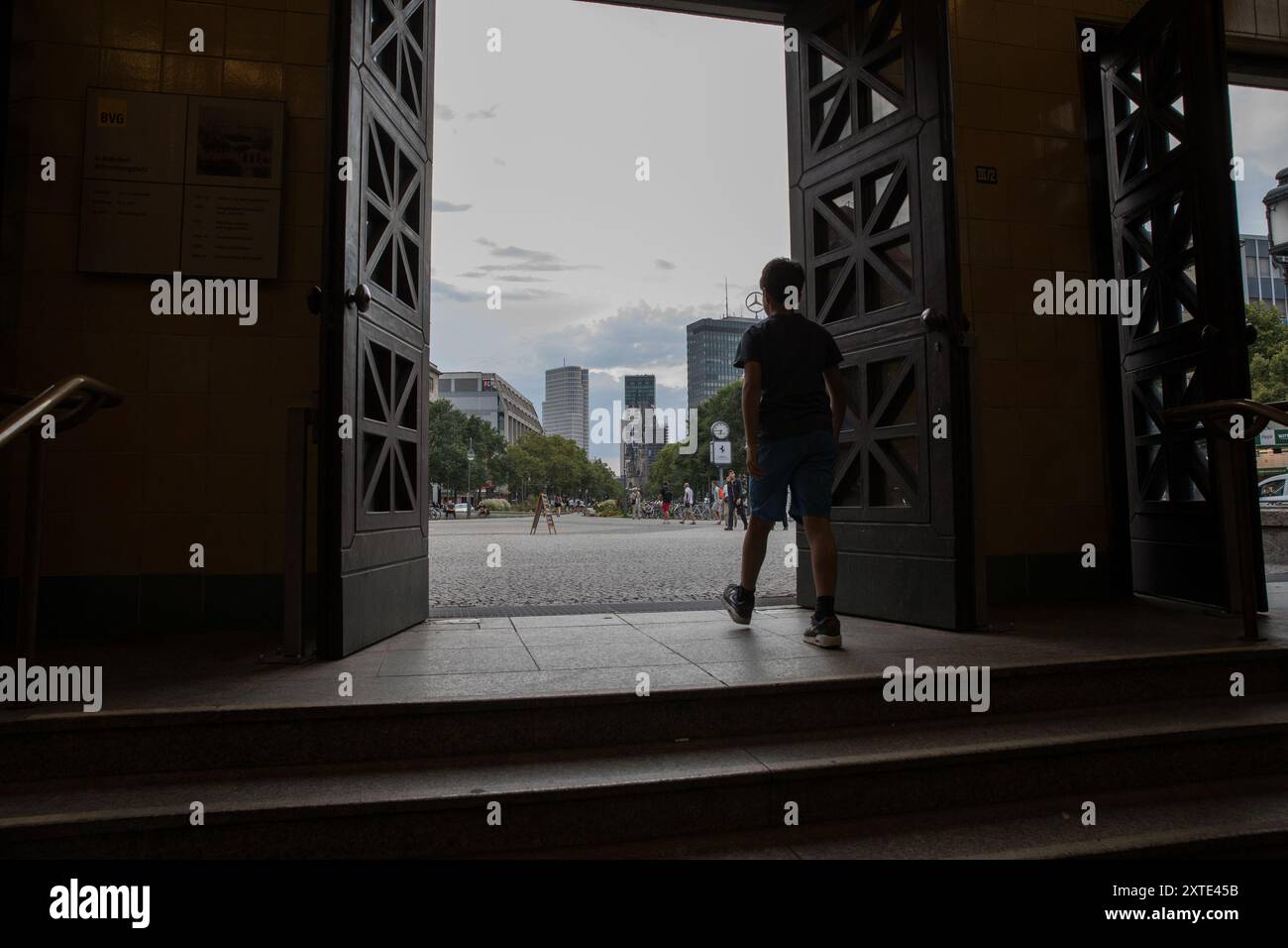 Berlin, Allemagne. 14 août 2024. Un jeune garçon entre sur la place animée de Wittenbergplatz à Berlin le 14 août 2024, encadrée par les portes ouvertes de la station de métro historique. Selon Eurostat, l'économie européenne a affiché une croissance modeste au printemps, le PIB de la zone euro ayant augmenté de 0,3% d'avril à juin par rapport au trimestre précédent. Toutefois, cette tendance positive ne s'est pas étendue à l'Allemagne, où le PIB a diminué de 0,1 %. L’économie allemande continue de se battre, avec des défis persistants qui ont retardé la reprise. (Crédit image : © Michael Kuenne/PRESSCOV via ZUMA Press Wi Banque D'Images