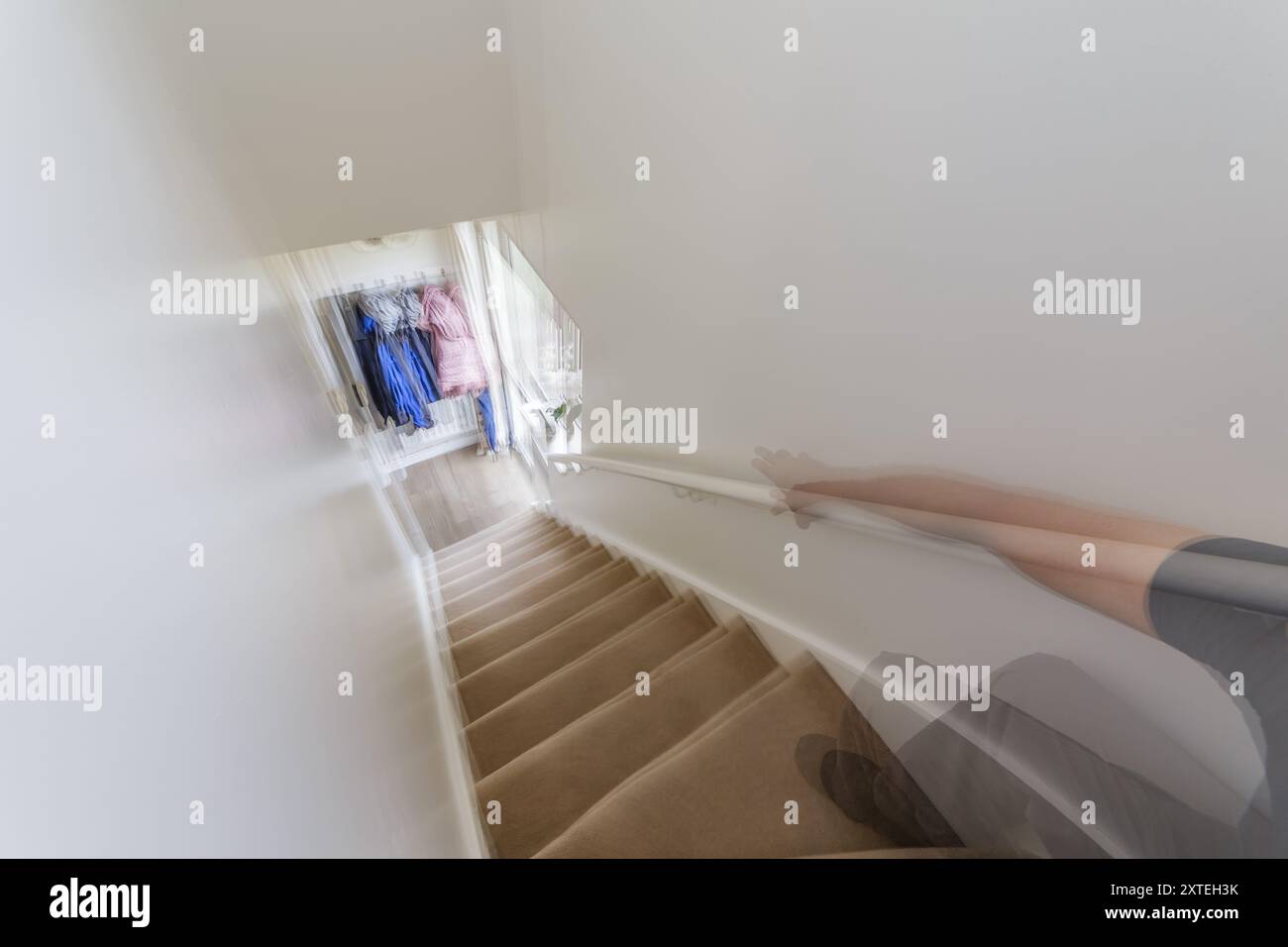 Une double exposition d'une prise de main courante, montrant un bras et une jambe de main ouverts flous menant à un escalier intérieur de la maison à un petit hall d'entrée. Banque D'Images