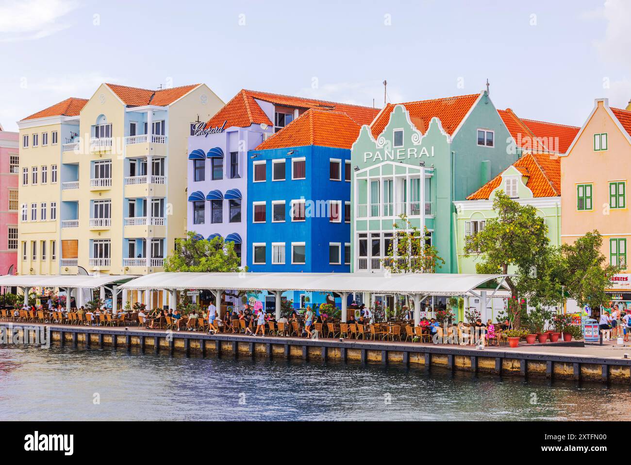 Bâtiments colorés en bord de mer à Willemstad, avec des restaurants en plein air le long de l'eau, offrant une atmosphère animée et vibrante les jours ensoleillés. Banque D'Images