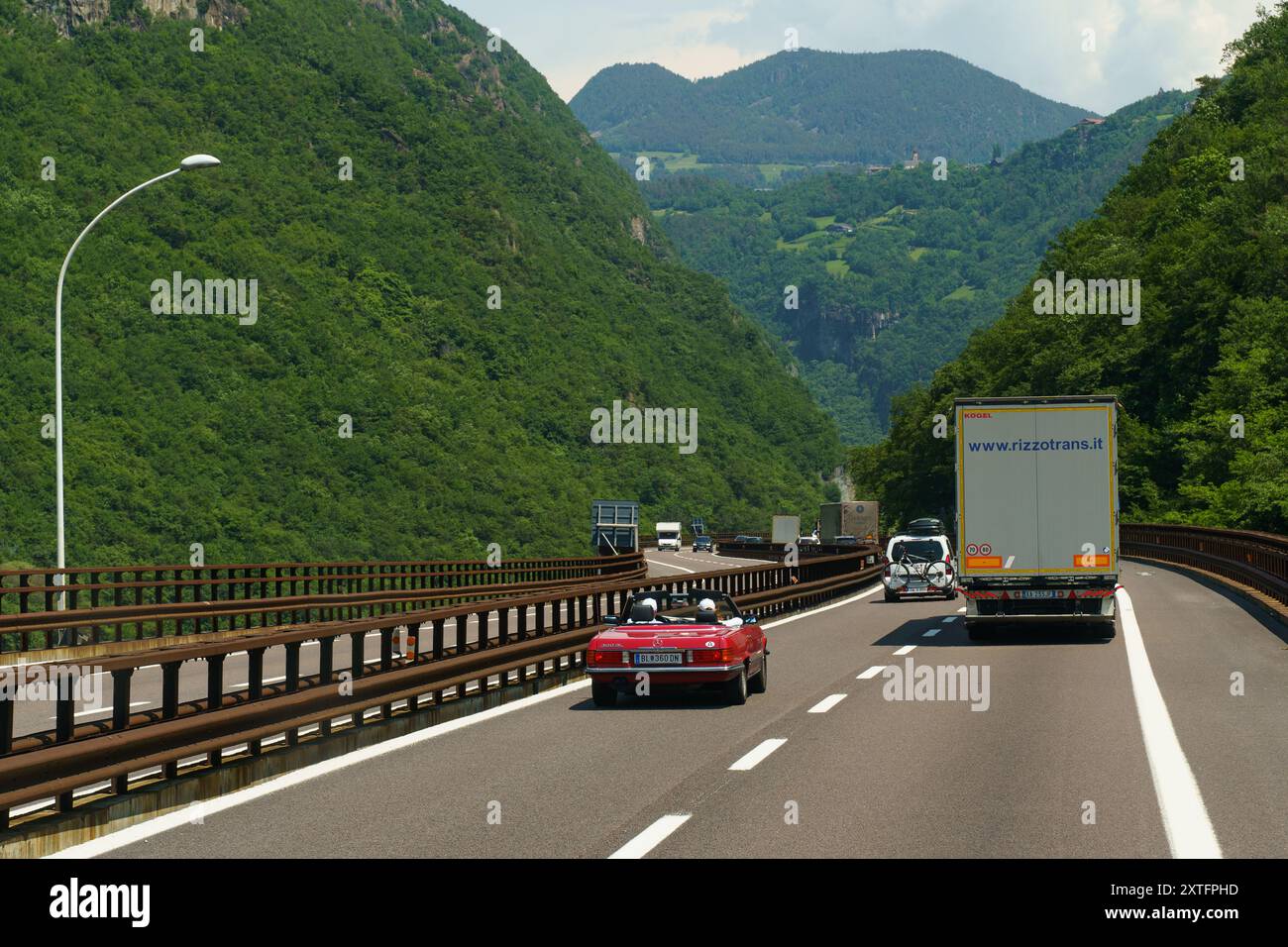 Bolzano, Italie - 8 juin 2023 : un cabriolet vole sur une autoroute pittoresque, flanquée de montagnes majestueuses et de verdure vibrante sous un bleu clair Banque D'Images