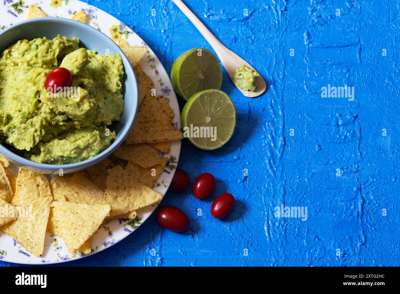 Version brésilienne de guacamole dans un bol bleu avec une tomate cerise sur le dessus entouré de nachos sur le dessus d'une table bleue. Banque D'Images