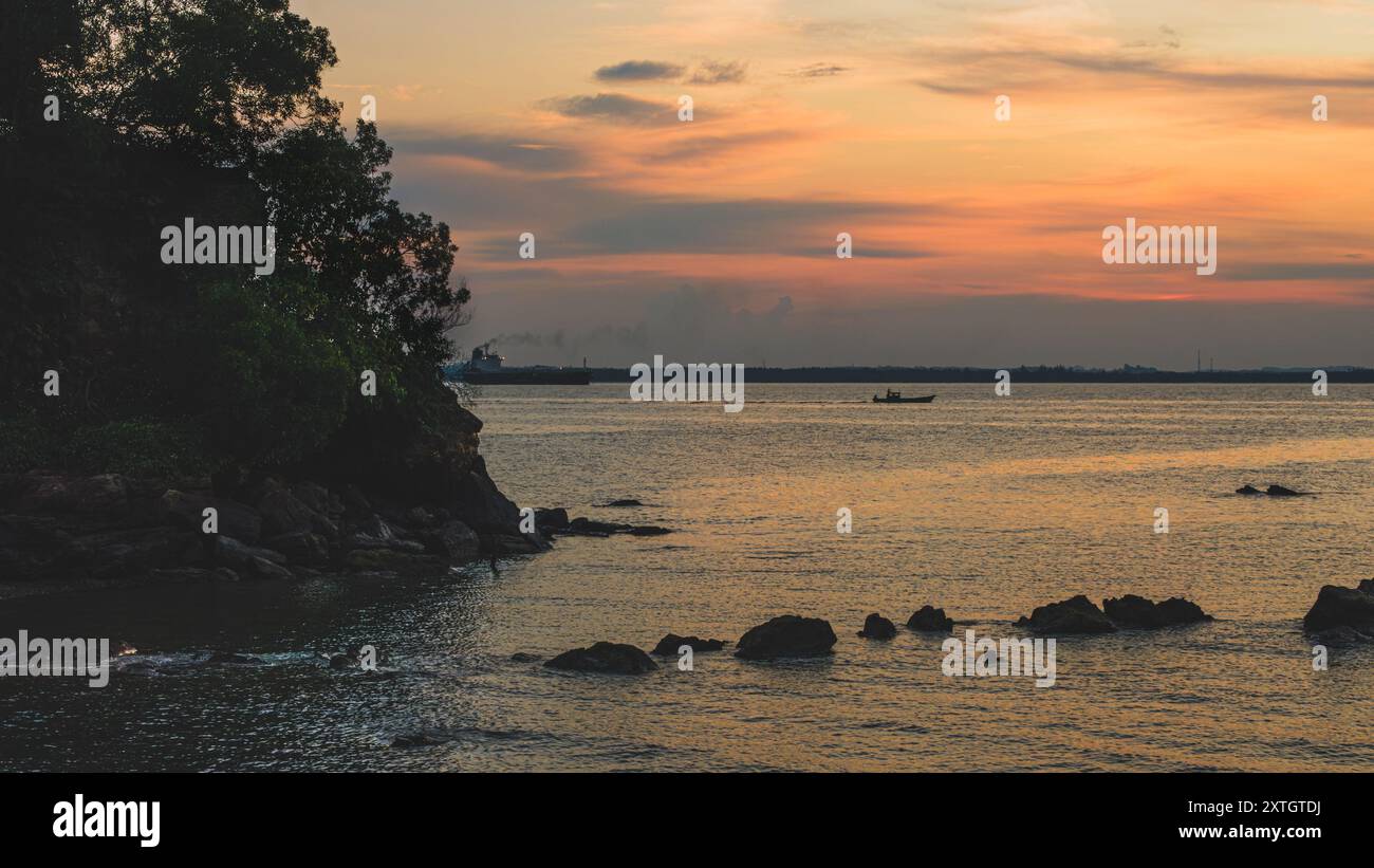 Balikpapan, Indonésie - 15 juin 2024. Une image tranquille d'un coucher de soleil vibrant sur la surface de l'océan, avec la silhouette d'un bateau et d'un navire. Banque D'Images
