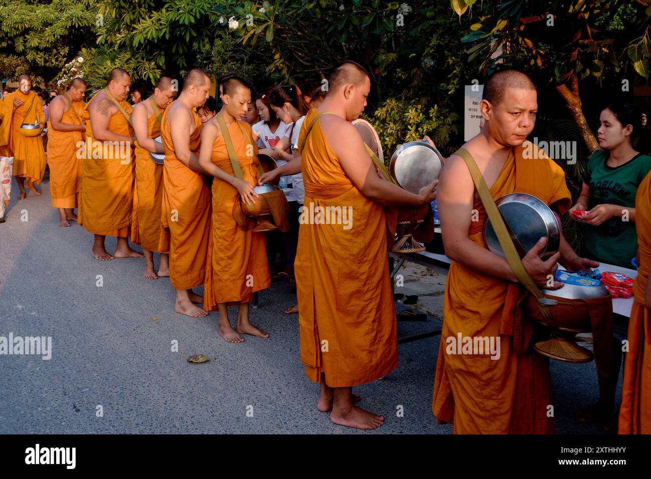 Lors d'un festival bouddhiste à Phuket, en Thaïlande, des moines bouddhistes oranges font la queue pour recevoir des dons de nourriture et de produits essentiels présentés par des laïcs Banque D'Images