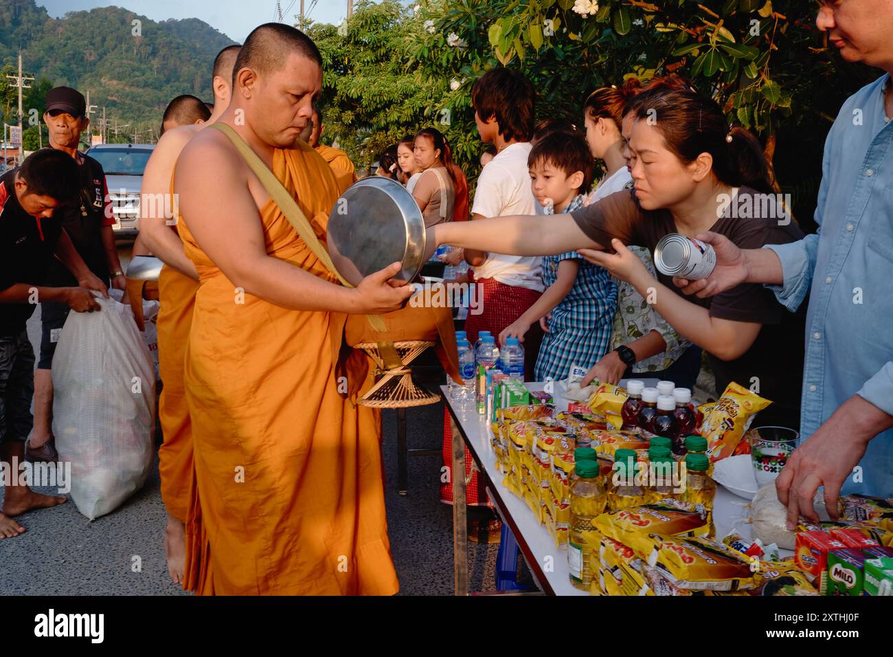 Lors d'un festival bouddhiste à Phuket, en Thaïlande, des moines bouddhistes oranges font la queue pour recevoir des dons de nourriture et de produits essentiels présentés par des laïcs Banque D'Images
