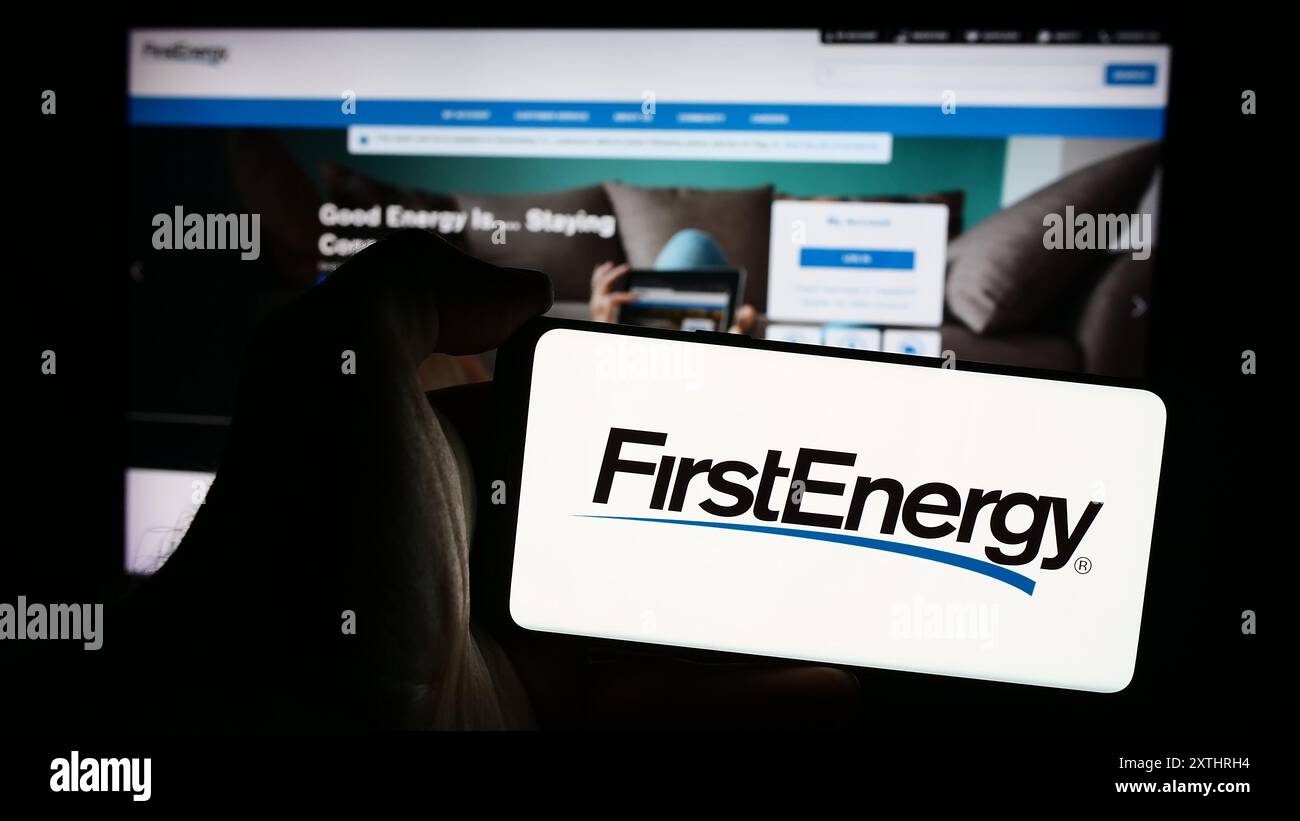 Personne tenant le téléphone portable avec le logo de la société américaine de services publics d'électricité FirstEnergy Corp. en face de la page Web. Concentrez-vous sur l'affichage du téléphone. Banque D'Images