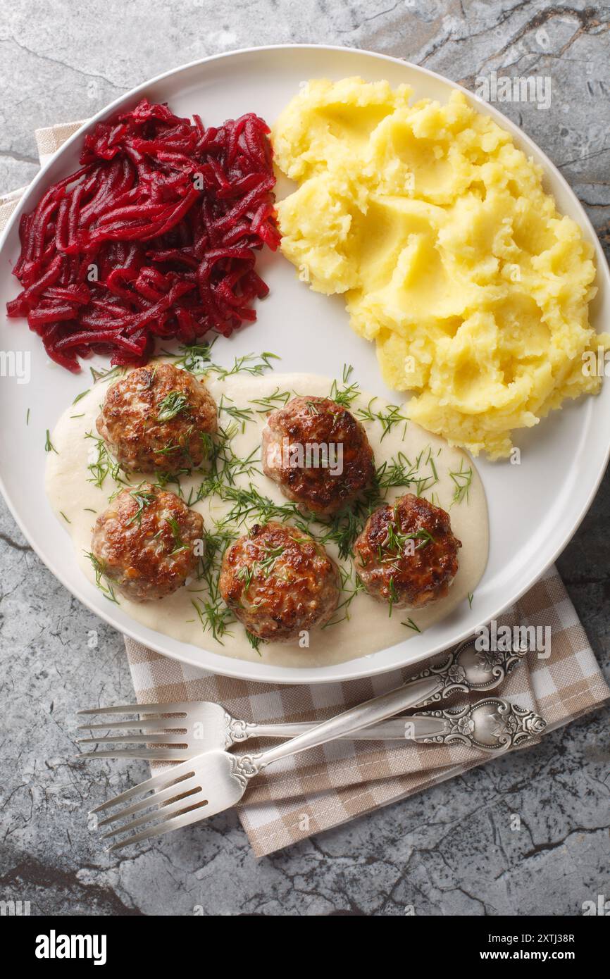 Portion de boulettes de viande avec sauce crémeuse avec purée de pommes de terre et salade de betteraves gros plan dans une assiette sur la table. Vue de dessus verticale Banque D'Images