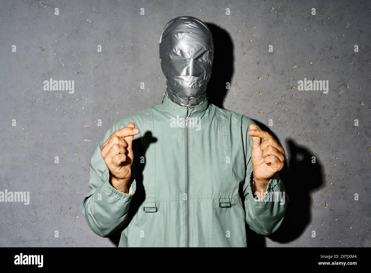 L'homme mystère avec le visage de bande de conduit fait mini symbole d'amour de coeur par les doigts sur fond gris Banque D'Images