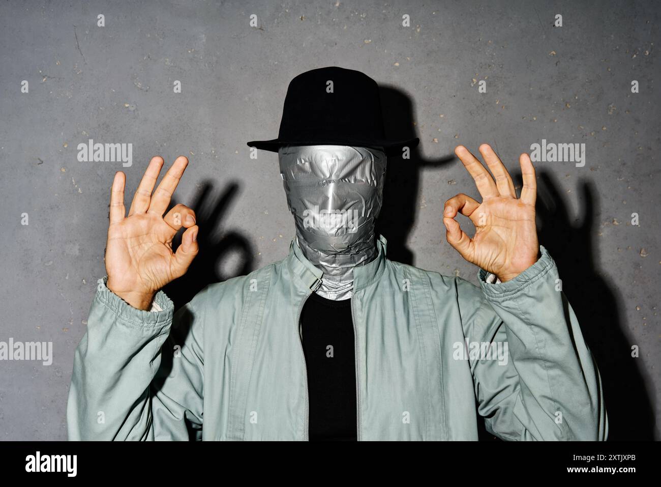 Homme mystère avec le visage de bande de conduit faisant signe OK avec la main et les doigts sur fond gris Banque D'Images