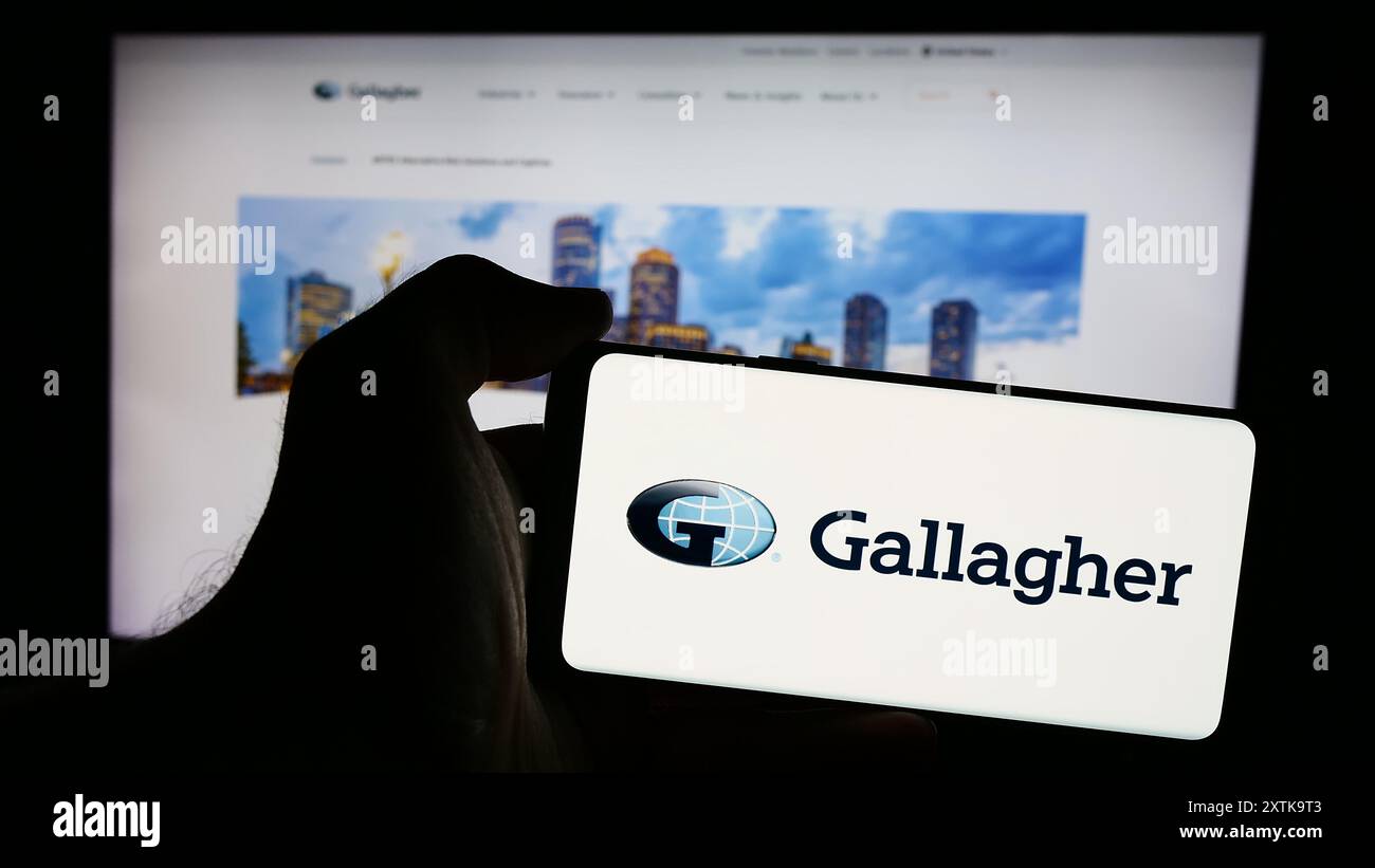 Personne tenant le téléphone portable avec le logo de la compagnie d'assurance américaine Arthur J. Gallagher Co. (AJG) en face de la page Web. Concentrez-vous sur l'affichage du téléphone. Banque D'Images