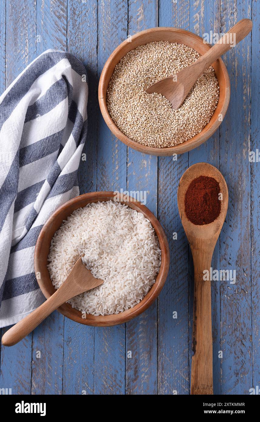 Bols en bois de riz et de quinoa sur une table bleue rustique avec une serviette de cuisine et une cuillère de paprika. Banque D'Images