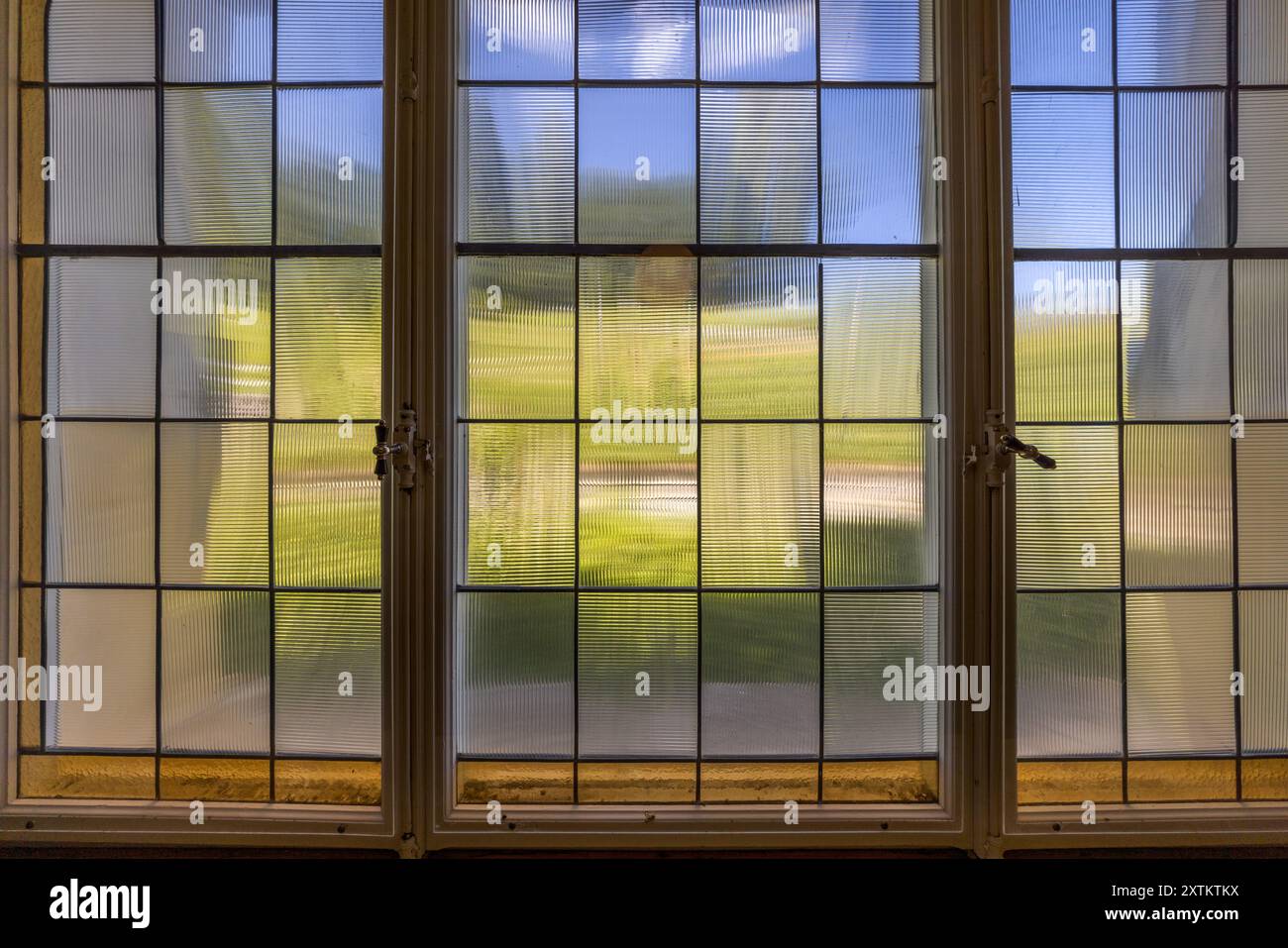 La Schatzalp au-dessus de Davos, Grisons, présente une fenêtre à meneaux en trois parties avec du verre texturé rainuré dans un couloir. À travers le verre texturé, seule une prairie verte et le ciel sont faiblement visibles. Otto Pfleghard et Max Haefeli ont construit l’ancien sanatorium entre 1898 et 1900 pour Willem Jan Holsboer, Bobbahnstrasse, Suisse. Banque D'Images