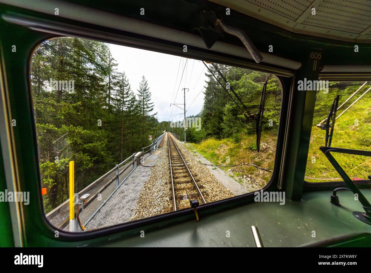 La locomotive de la Rhétienne Ge 4/4 I n° 605 'Silvretta' tire son train historique autour d'un virage à travers une forêt dense, vue depuis la plateforme ouverte de la cabine sur la ligne de l'Albula, Grisons. Le numéro 605 est marqué sur le mur de la cabine. Mise en service en 1953, la locomotive est l'une des dix de cette classe construites entre 1947 et 1953, chacune nommée d'après une vallée ou un paysage des Grisons. La ligne de l'Albula fait partie du site du patrimoine mondial de l'UNESCO 'Chemin de fer rhétien dans les paysages de l'Albula/Bernina' depuis 2008, Bahnhofstrasse, Davos, Suisse. Banque D'Images