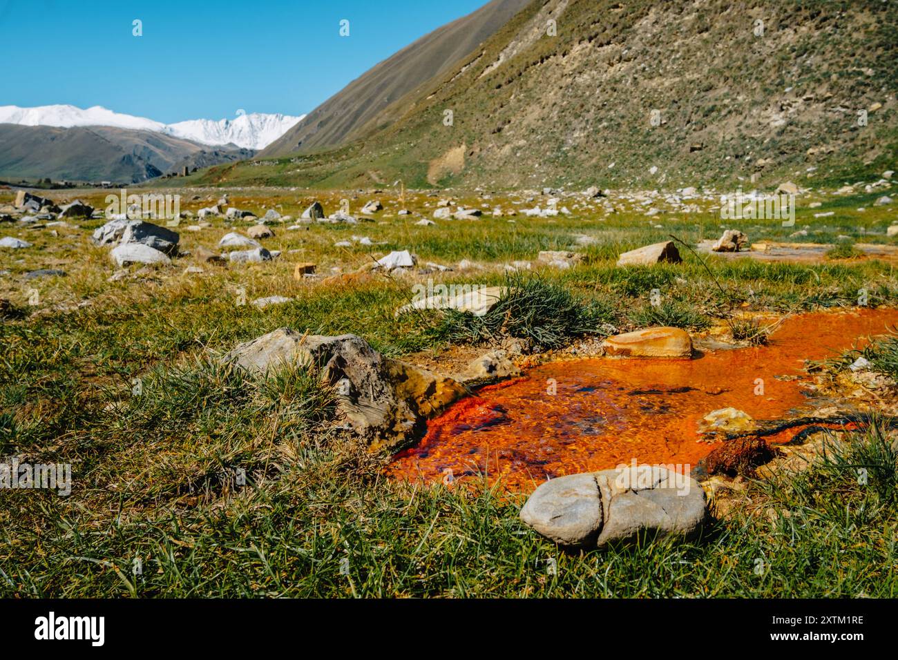 Flaque d'eau riche en fer orange dans la gorge de Truso avec des sommets enneigés en arrière-plan près de Kazbegi, Géorgie Banque D'Images