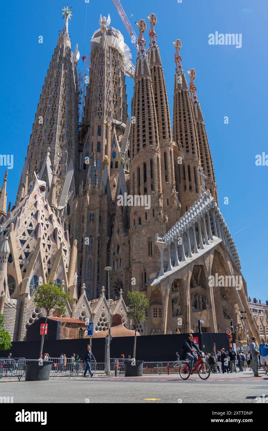 Barcelone, Espagne - 19 avril 2024 : la cathédrale de la Sagrada Familia au printemps avec un chauffeur de vélo et un touriste Banque D'Images
