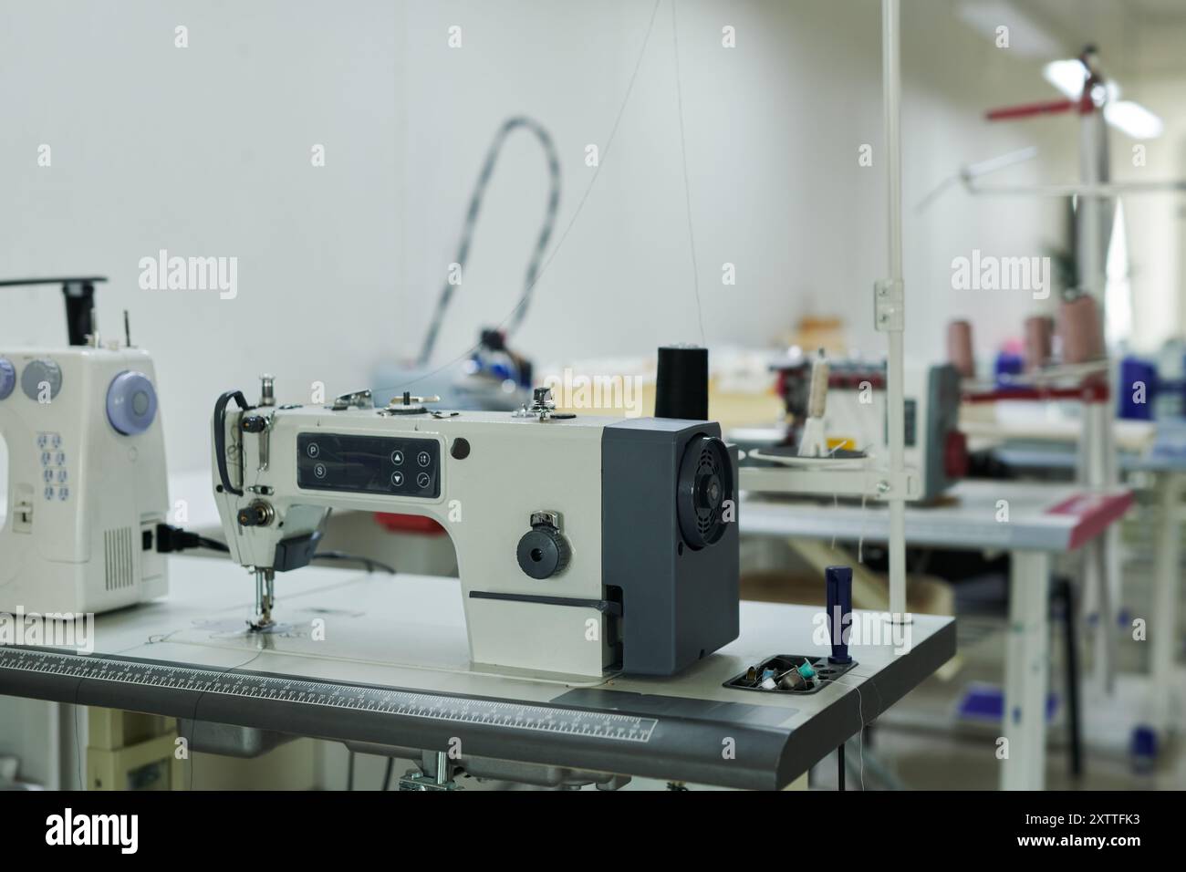 Rangée de bureaux avec machines à coudre électriques et autres équipements de couture debout dans un atelier ou atelier moderne spacieux Banque D'Images