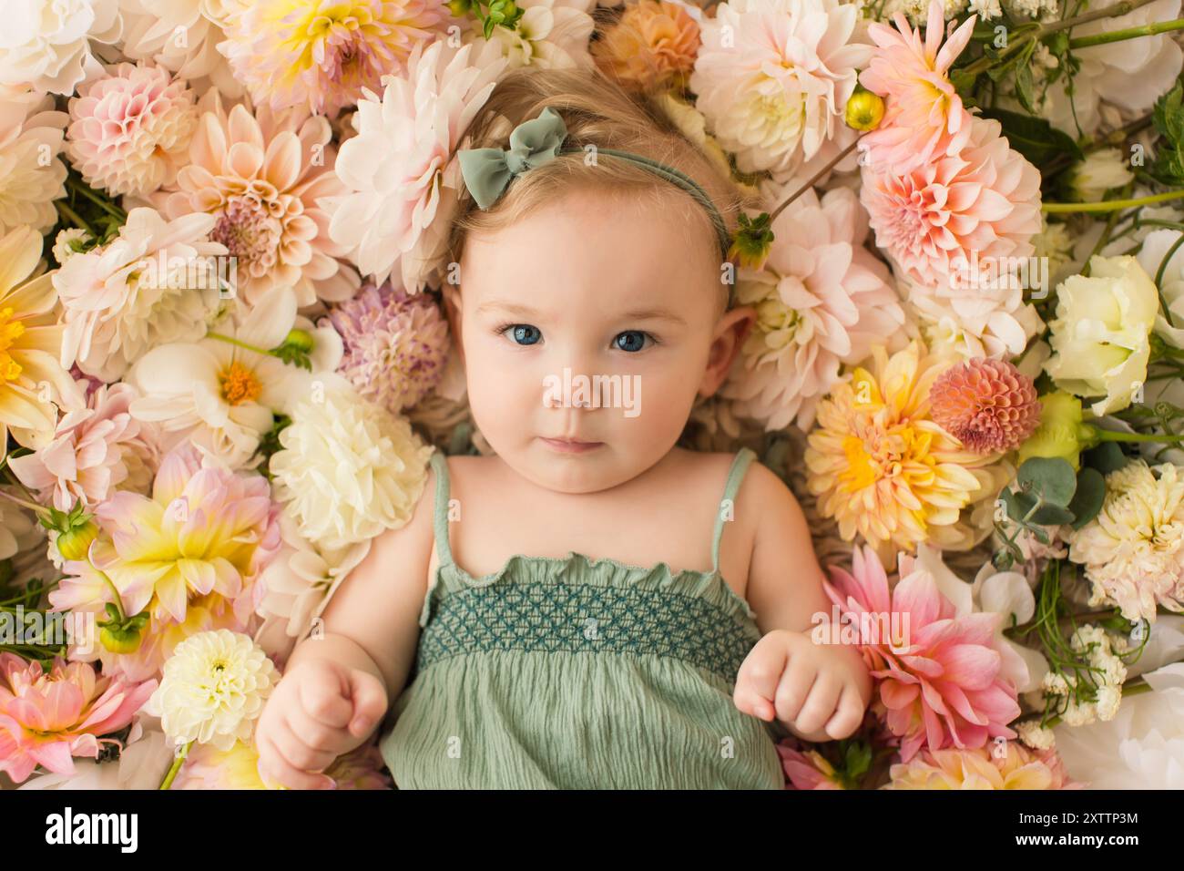 Bébé avec les yeux bleus couché sur un lit de fleurs colorées, portant Banque D'Images