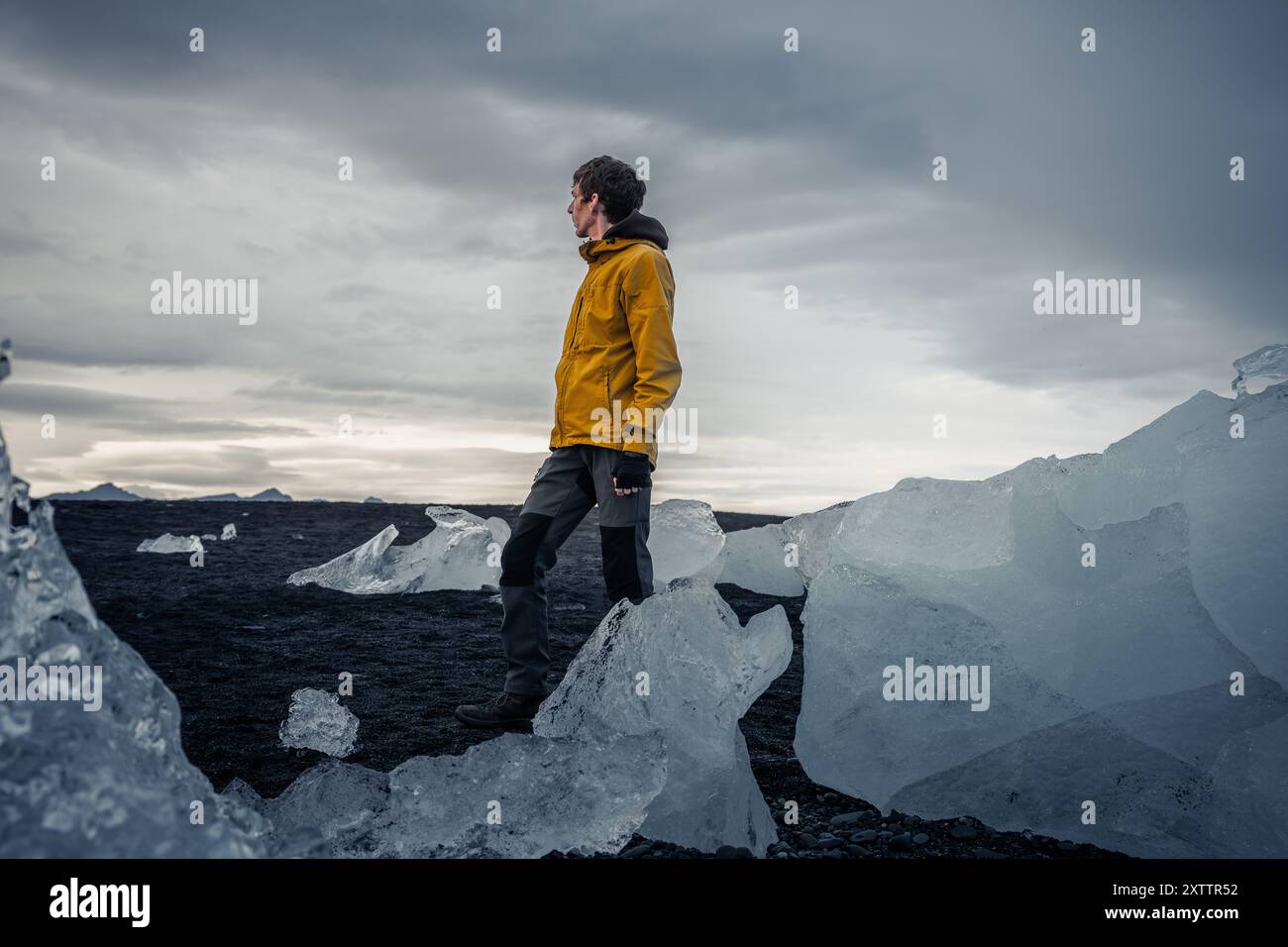 Jeune homme en veste jaune se tient à Diamond Beach, Islande Banque D'Images