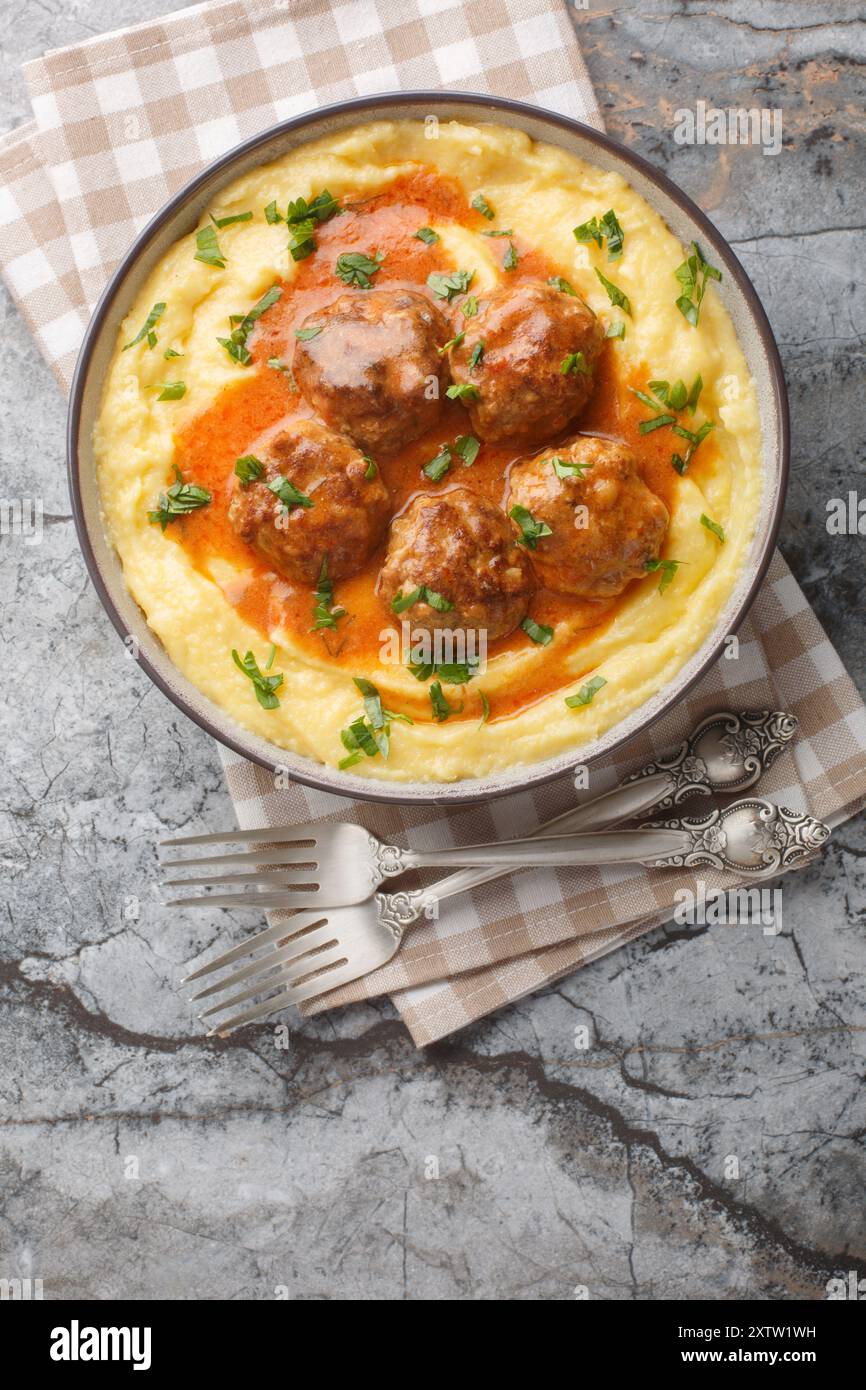 Boulettes de viande avec sauce épicée avec un plat d'accompagnement de porridge de maïs gros plan dans un bol sur la table. Vue de dessus verticale Banque D'Images