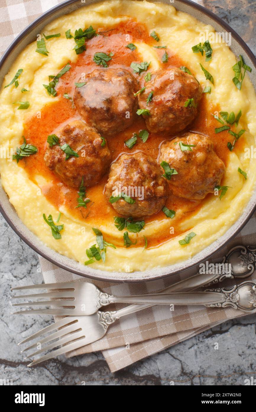Polenta de maïs à la crème et au fromage servi avec des boulettes de viande dans une sauce épicée gros plan dans un bol sur la table. Vue de dessus verticale Banque D'Images