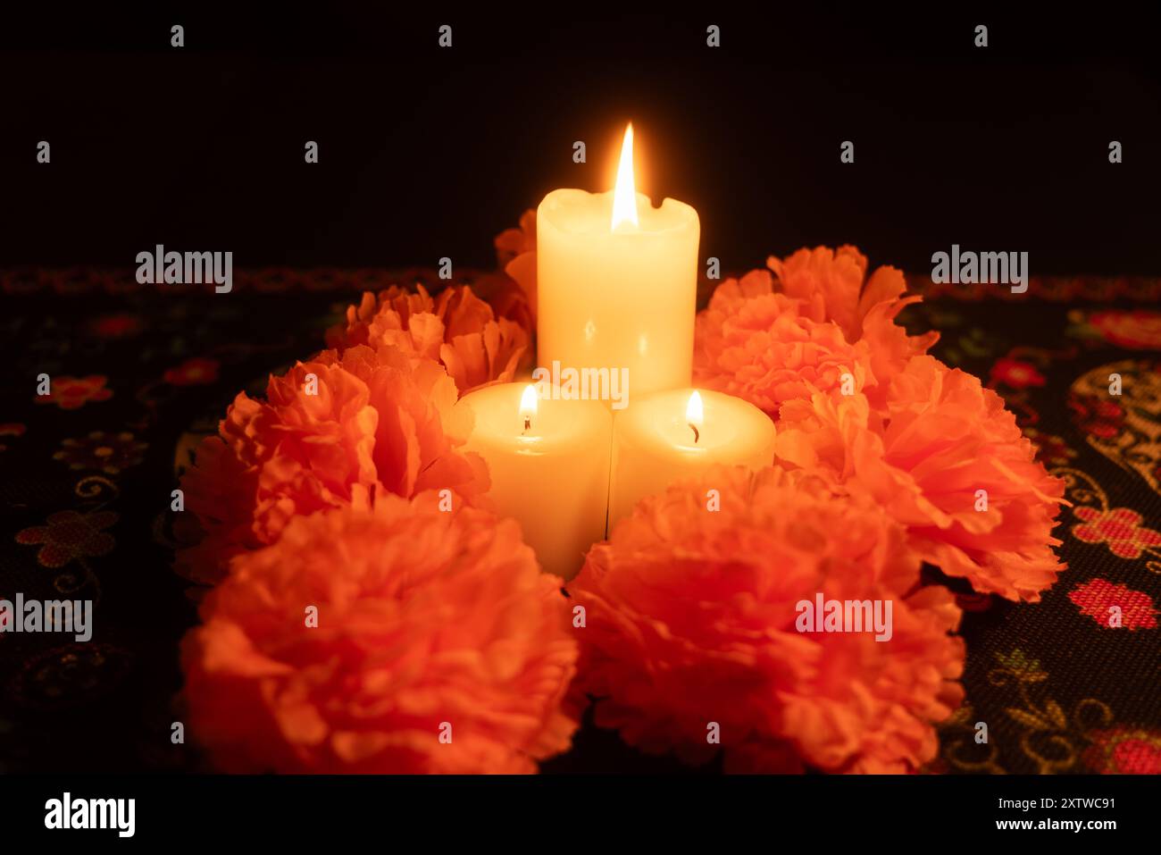 Une vue générale de trois bougies allumées au centre, entourées de soucis orange vibrants. Placé sur un fond noir, la scène est éclairée de sorte Banque D'Images