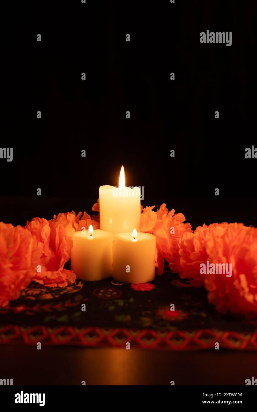 Une photo verticale avec trois bougies allumées au centre de l'image, entourées de soucis orange vifs. La scène est éclairée par des chandelles Banque D'Images