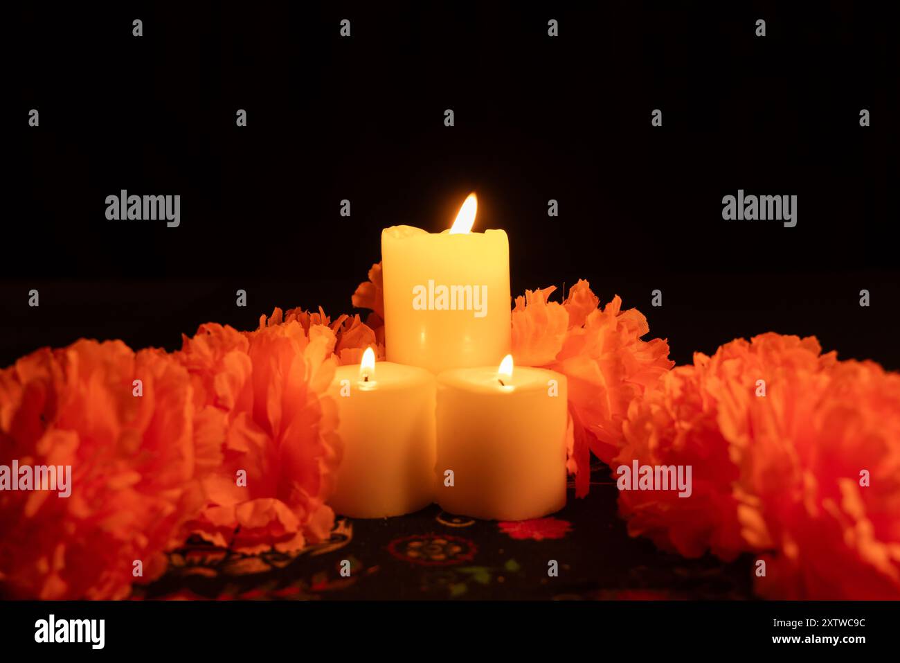 Plan vertical avec trois bougies allumées au centre, entourées de marigolds orange vifs. La scène, éclairée uniquement par la lumière des bougies, repose sur Banque D'Images