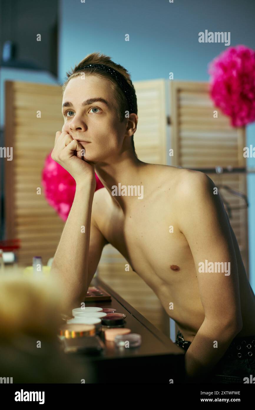 Une drag queen est assise à une coiffeuse, appuyée sur leur main, et regarde au loin, apparemment perdue dans ses pensées. Banque D'Images