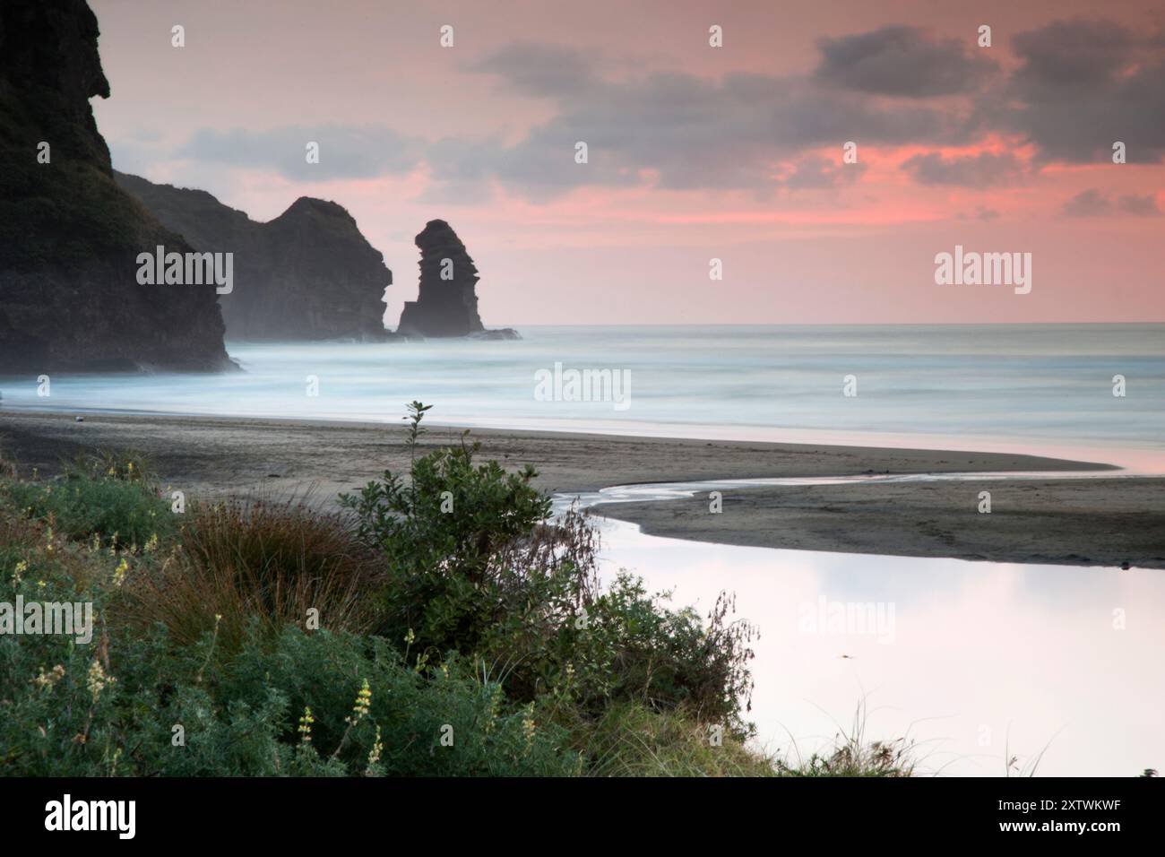 Plage tranquille au crépuscule avec des eaux calmes, une formation rocheuse au loin sous un ciel pastel. Banque D'Images Plage tranquille au crépuscule avec des eaux calmes, une formation rocheuse au loin sous un ciel pastel. Banque D'Images