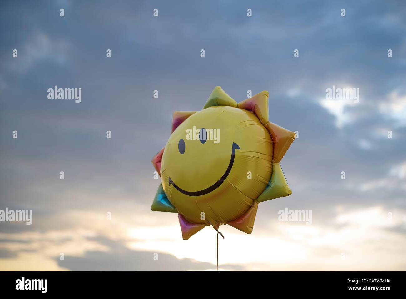 Un ballon en forme de soleil éclatant avec un visage souriant flotte contre un ciel crépusculaire serein. Banque D'Images