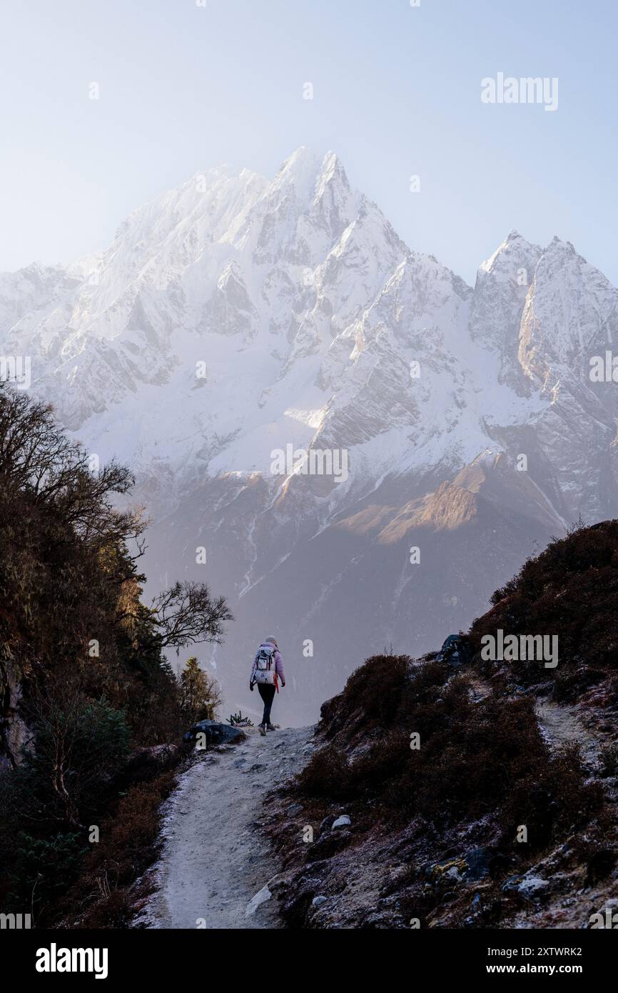 Un randonneur marche sur un sentier de montagne avec de majestueux sommets enneigés en arrière-plan sous un ciel dégagé. Banque D'Images
