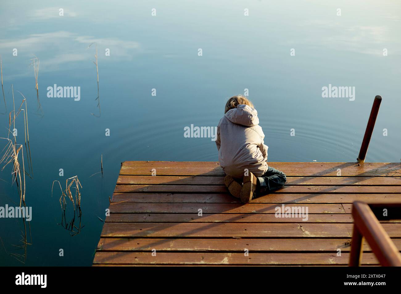 Une personne s'agenouille sur un quai en bois au-dessus de l'eau calme, regardant sur le lac serein pendant un moment calme. Banque D'Images