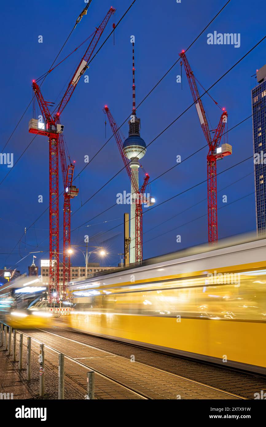La célèbre tour de télévision de Berlin la nuit avec des grues de construction rouges et un tramway flou de mouvement Banque D'Images