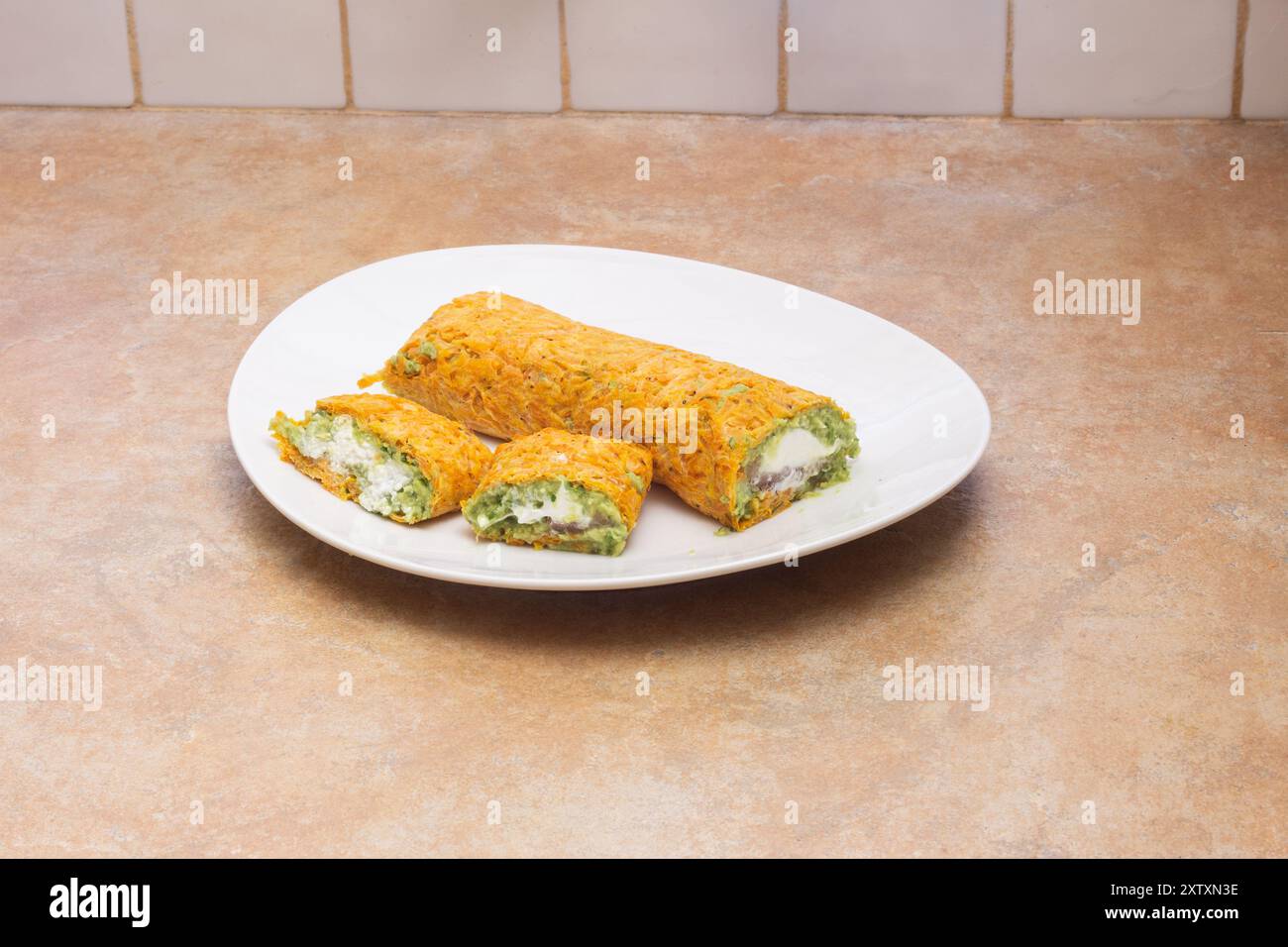 Une assiette de délicieux rouleaux de carottes faits maison remplis de fromage ricotta crémeux et de guacamole frais, sertis sur un comptoir de cuisine beige propre avec carrelage Banque D'Images