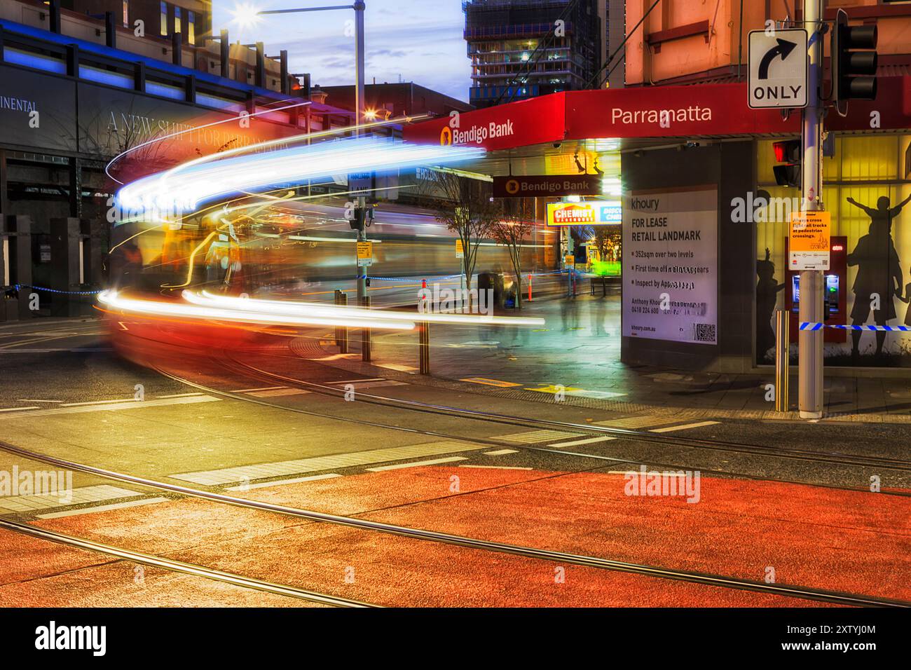 Sydney, Australie - 20 juin 2024 : coin de rue dans la ville de Parramatta au coucher du soleil avec la nouvelle ligne de tramway léger floue longue exposition. Banque D'Images