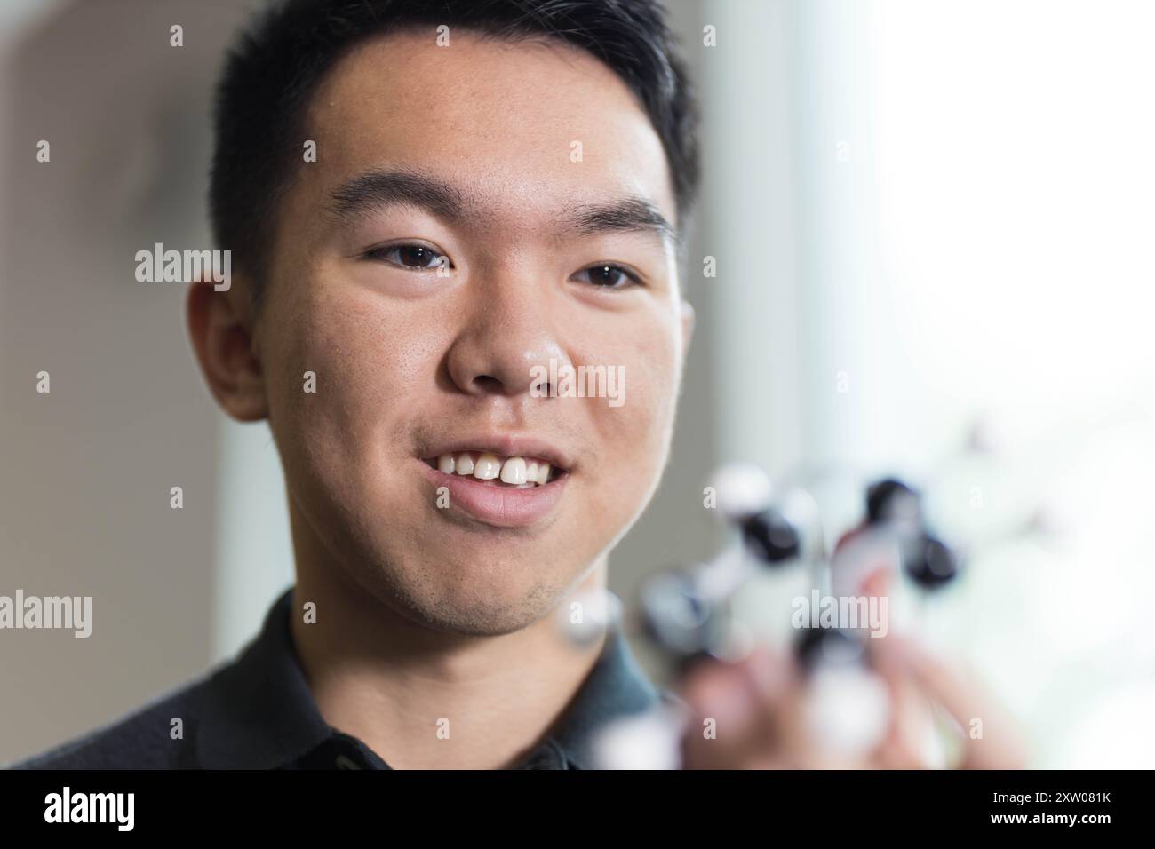 Un jeune étudiant universitaire masculin tenant un modèle d'une molécule dans sa main, intéressé par la science dans la classe gros plan portrait Banque D'Images