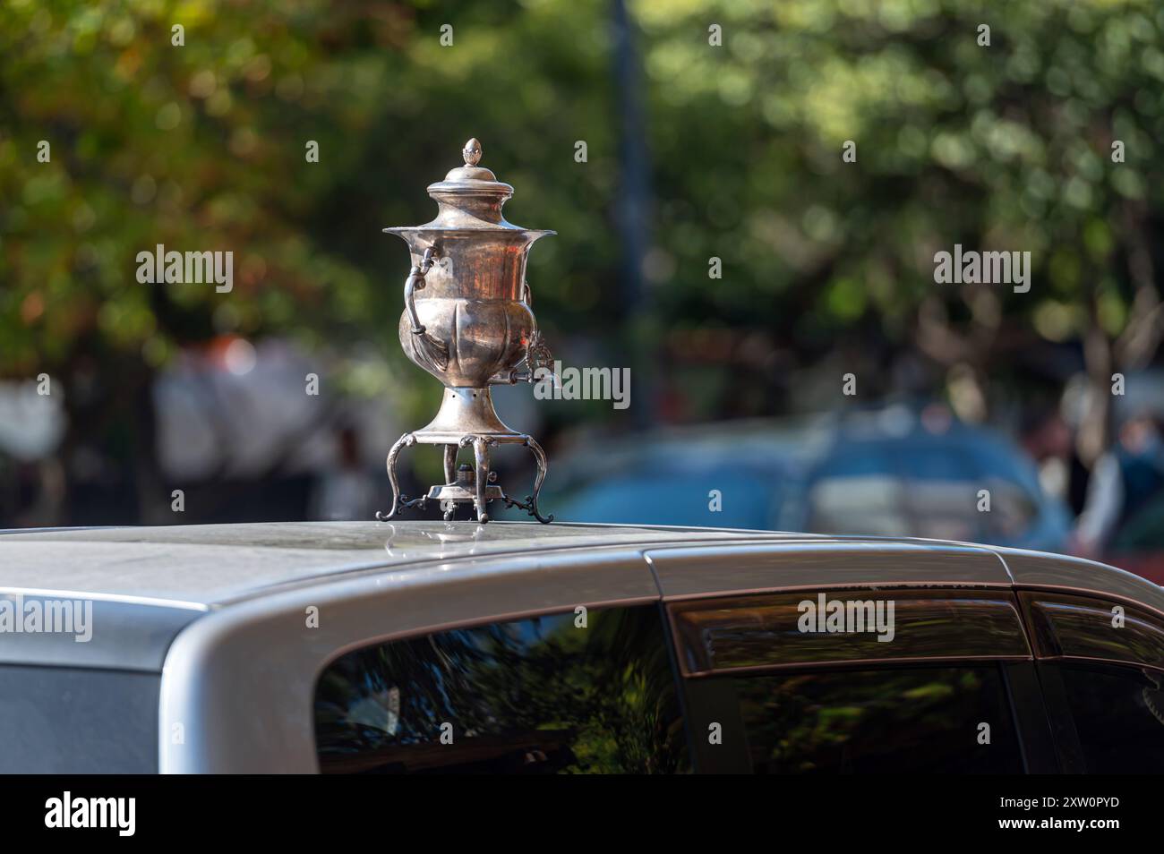Un samovar décoratif argenté repose au sommet d'une voiture garée dans un quartier animé de la ville. Banque D'Images