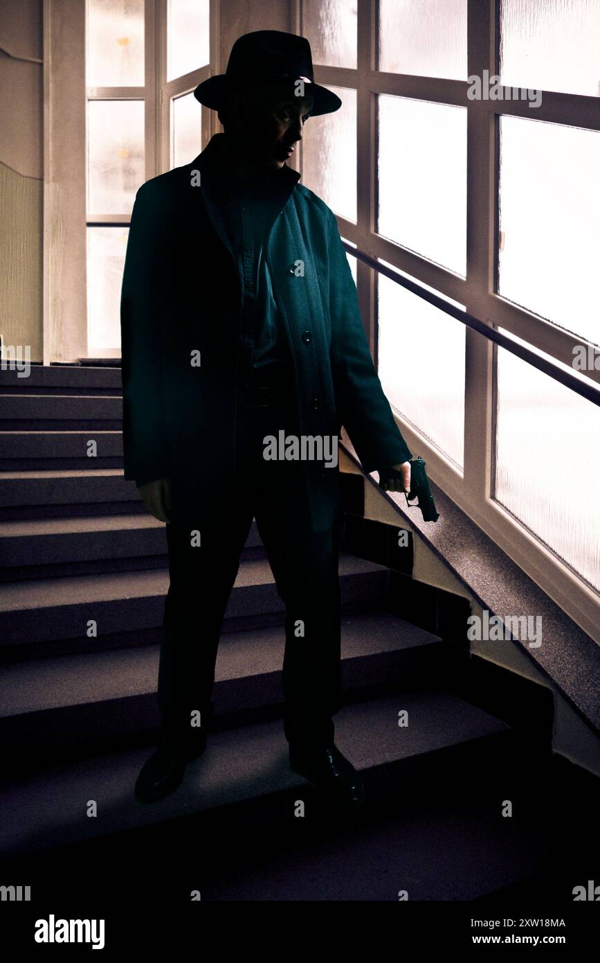 homme portant un chapeau fedora et tenant une arme à feu à l'intérieur d'un bâtiment Banque D'Images